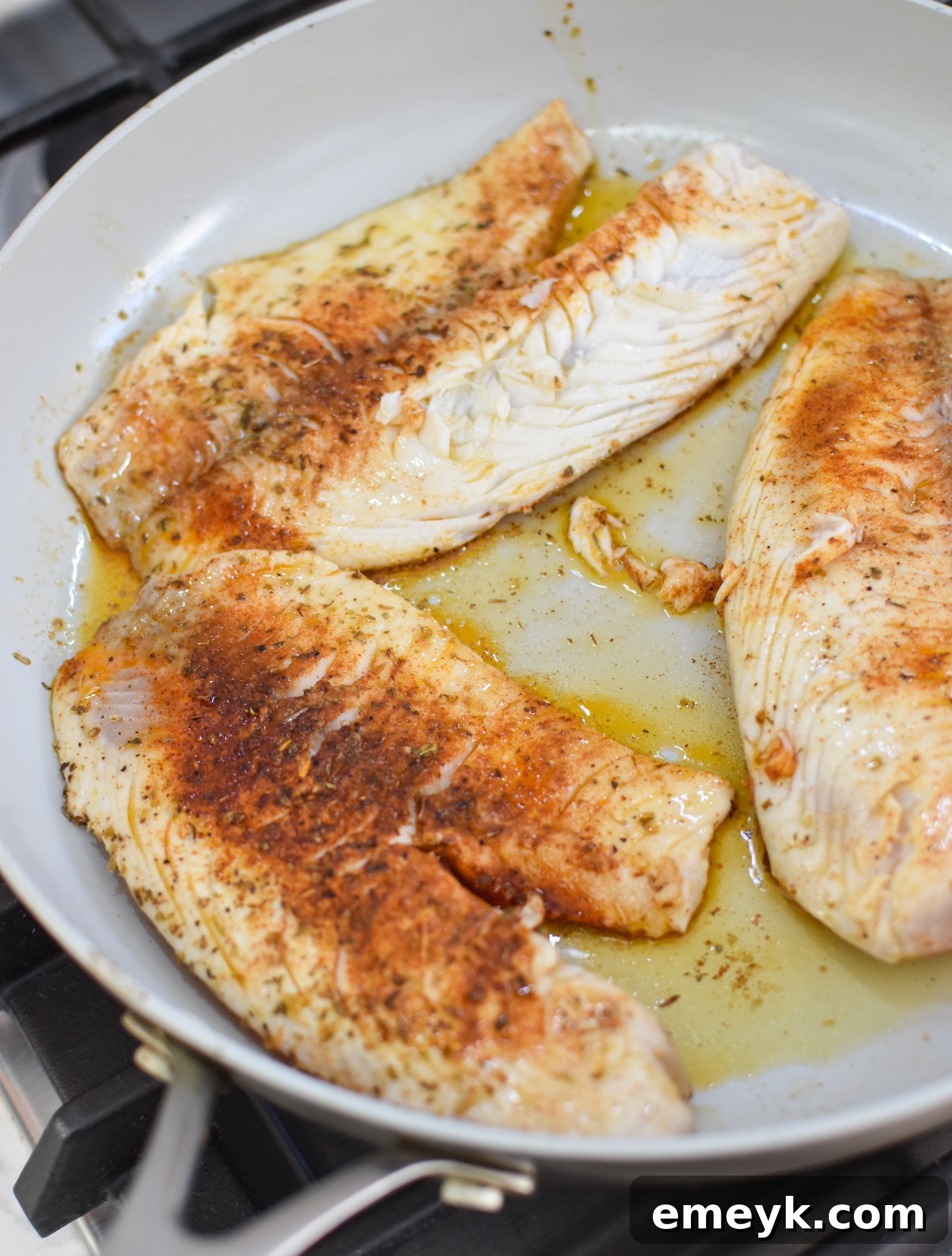 Tilapia fillets searing in a hot skillet with spices and olive oil.