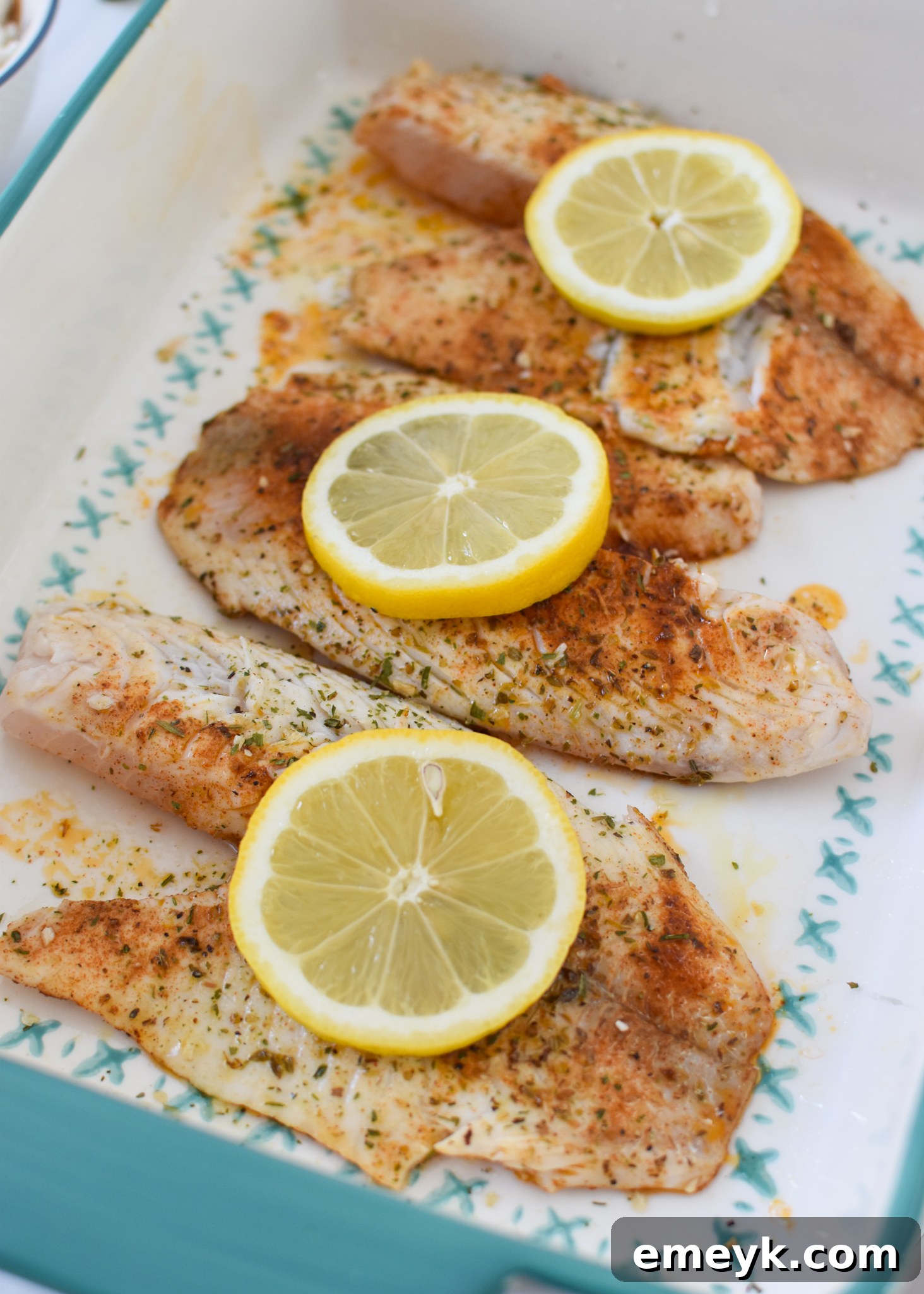 Greek Baked Tilapia fillets with lemon slices in a pan, ready for the oven.