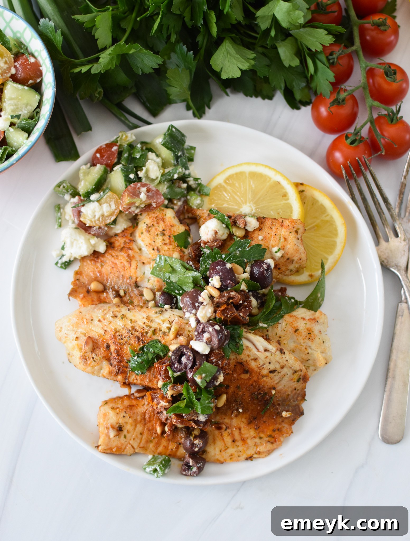 Plated Greek Baked Tilapia with olive tapenade, lemon, and a side of Mediterranean chopped salad.