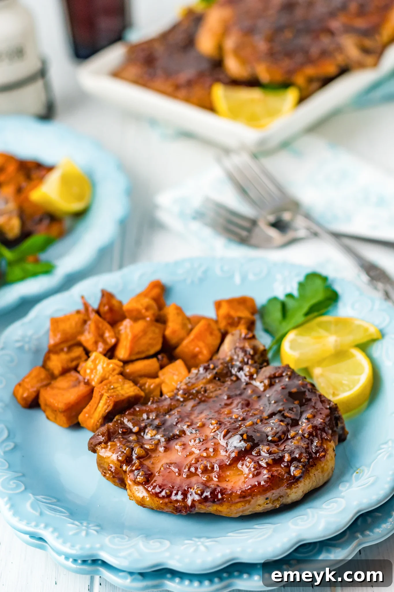 Sweet and sticky Maple Bourbon Pork Chops served on a blue plate alongside roasted sweet potatoes, a perfect dinner meal.