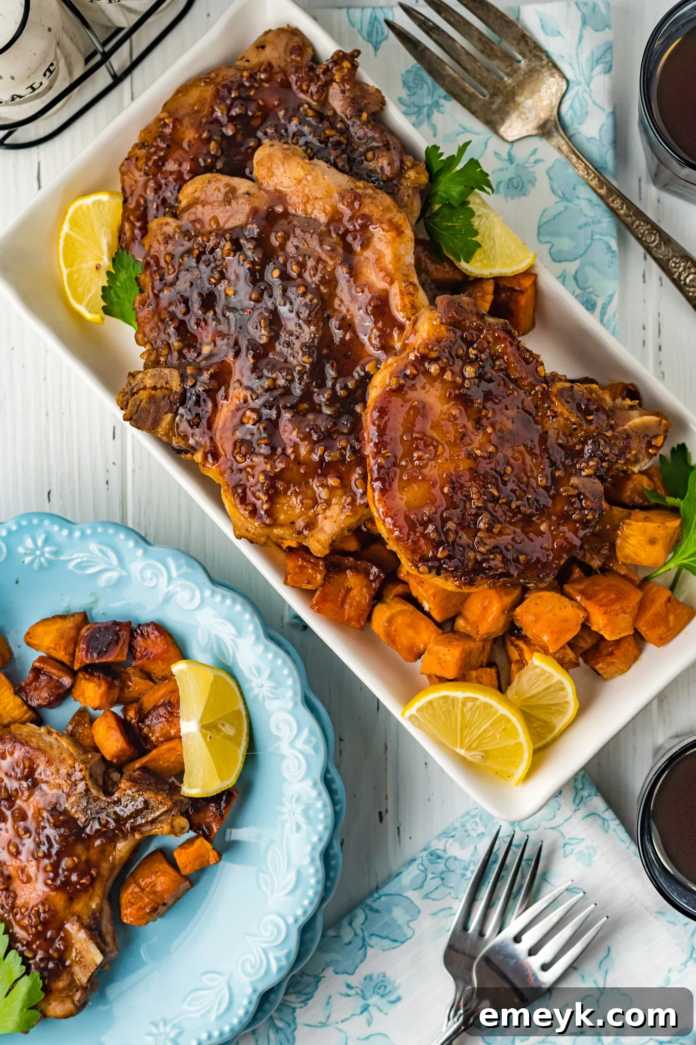 A large platter of Maple Bourbon Pork Chops and roasted sweet potatoes, garnished and ready for serving family style.