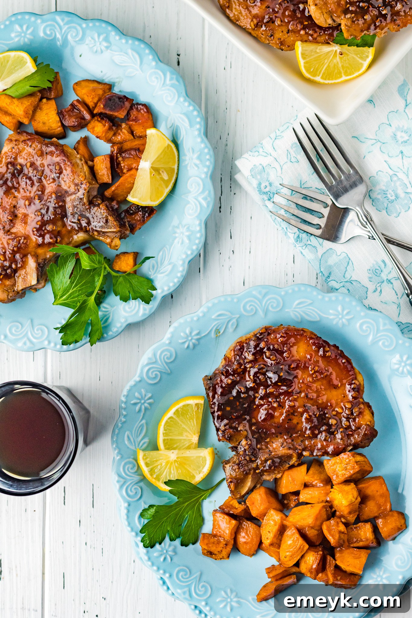 Two plates of Maple Bourbon Pork Chops with roasted sweet potatoes, elegantly presented.