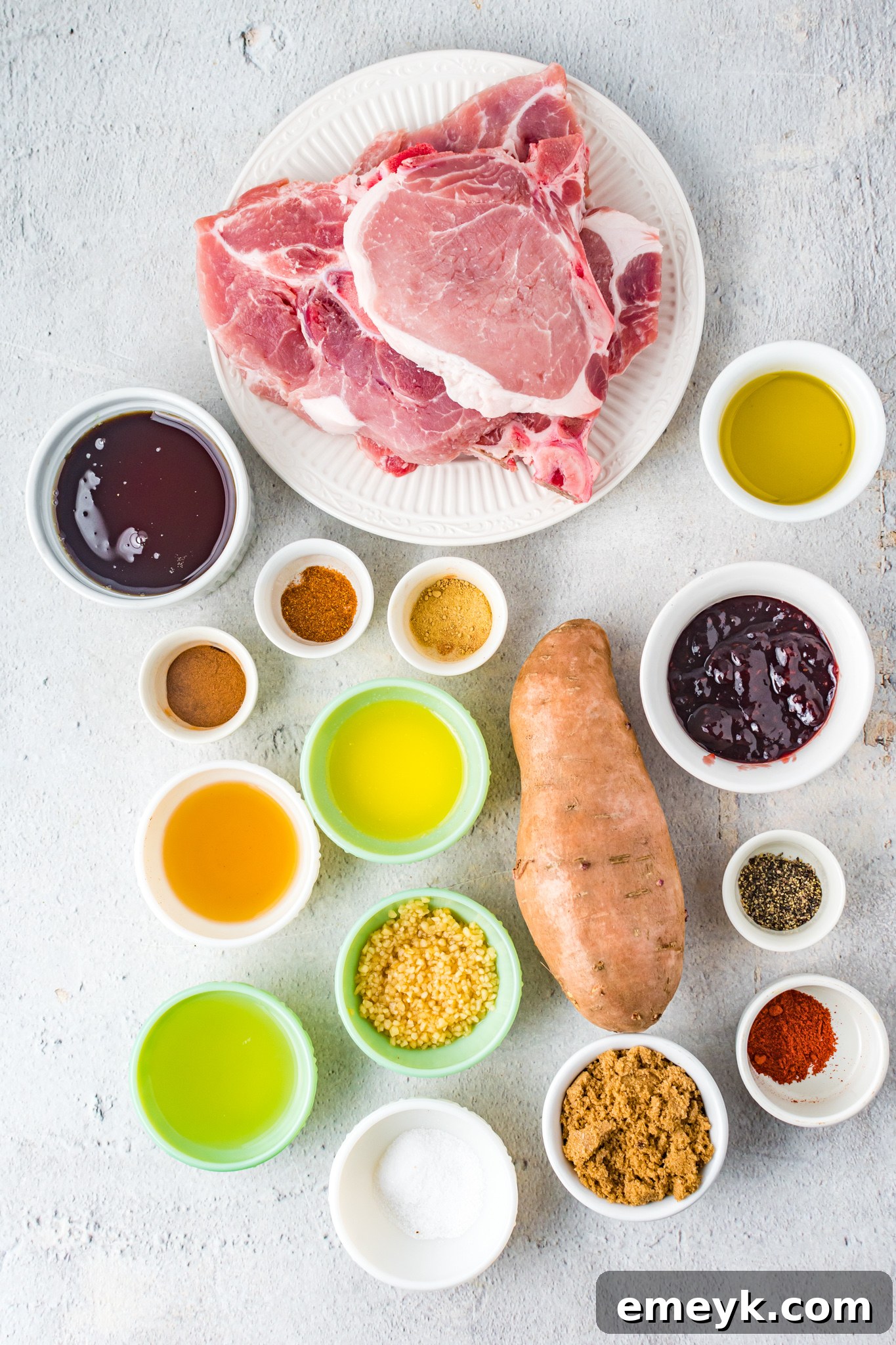 Assortment of fresh ingredients for Maple Bourbon Pork Chops Recipe laid out on a wooden surface, including pork chops, sweet potatoes, maple syrup, bourbon, and spices.