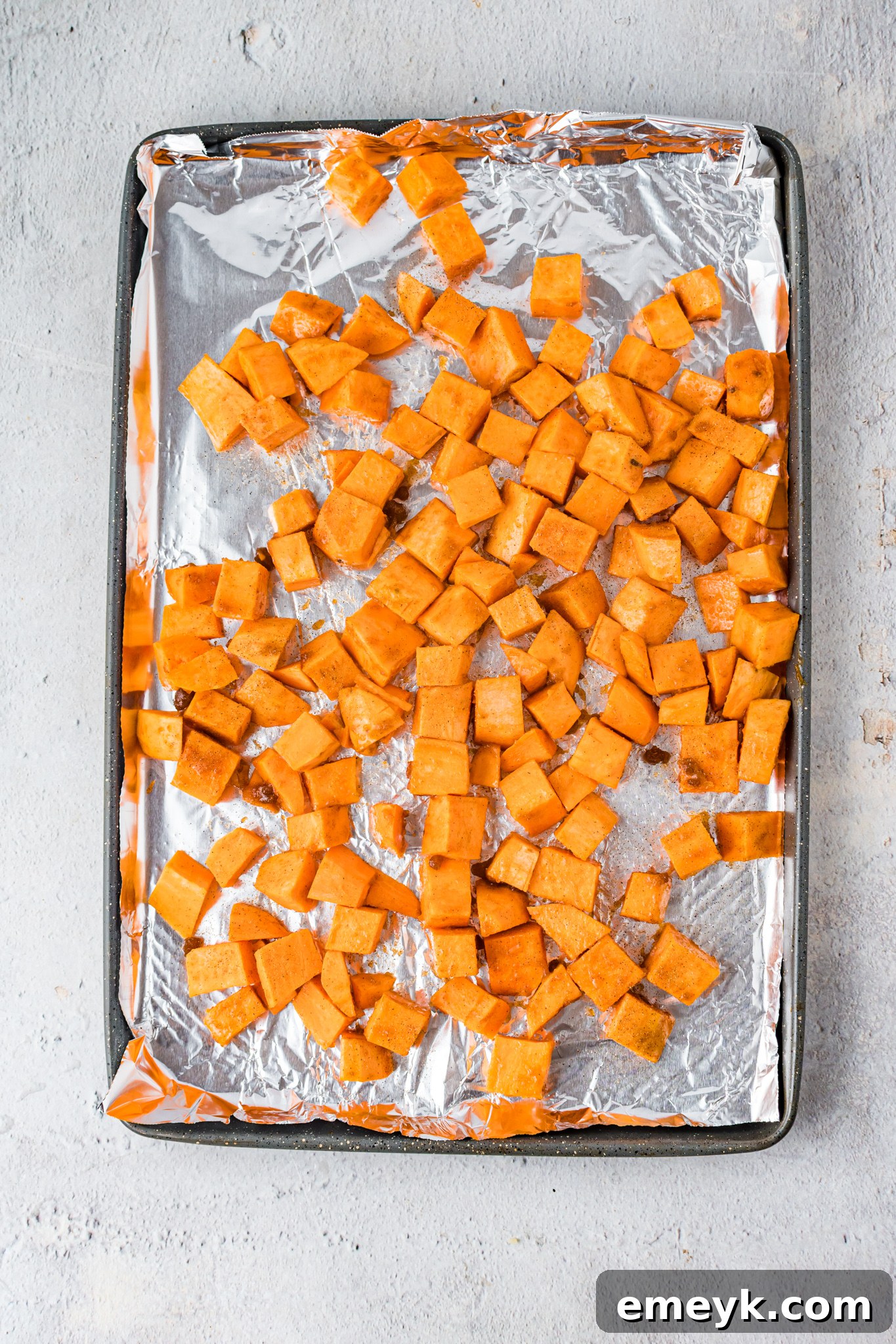 Sweet potatoes coated in a maple-brown sugar glaze on a baking sheet, ready for roasting.