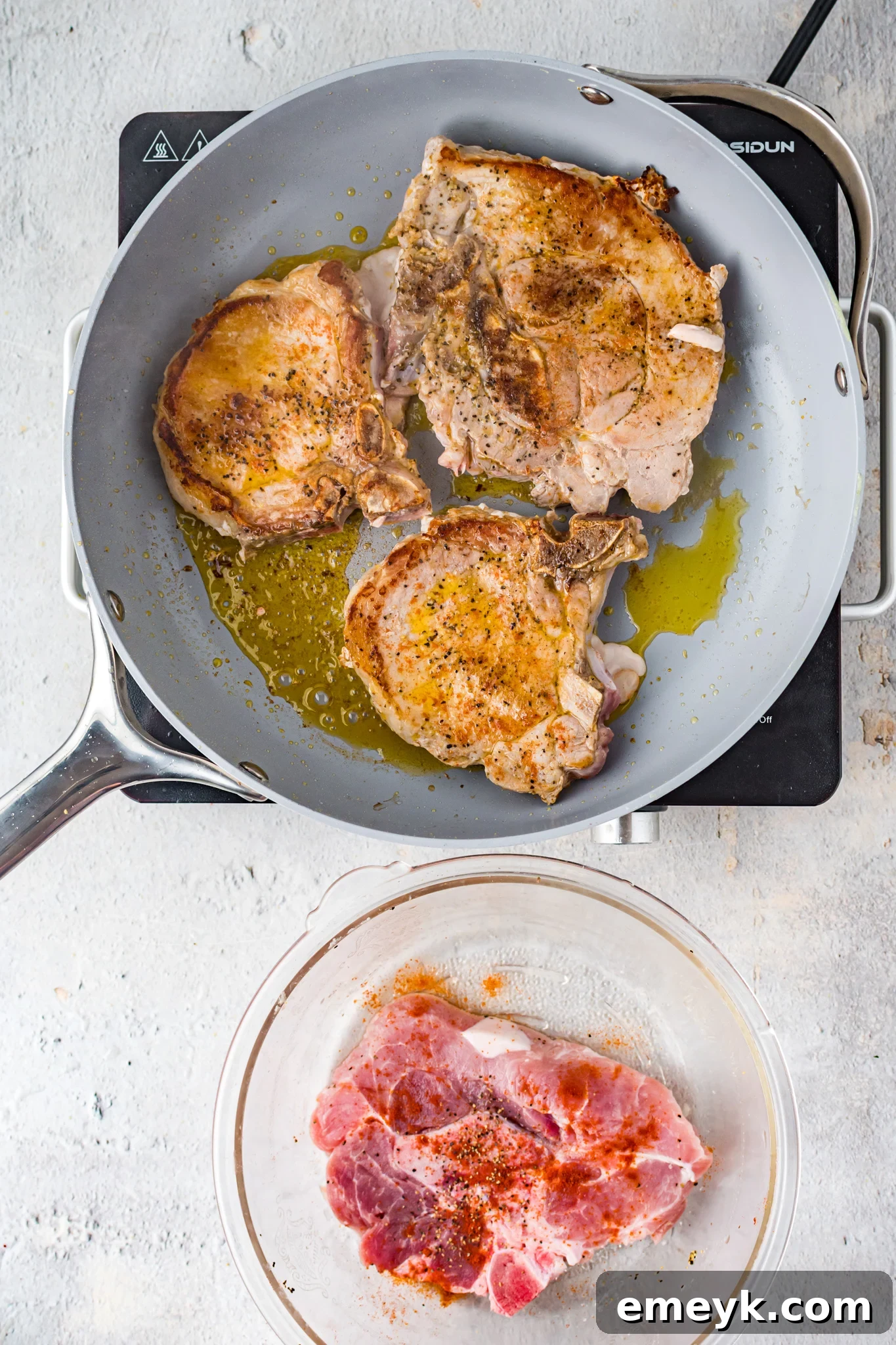 Pork chops searing in a hot skillet, developing a golden crust.