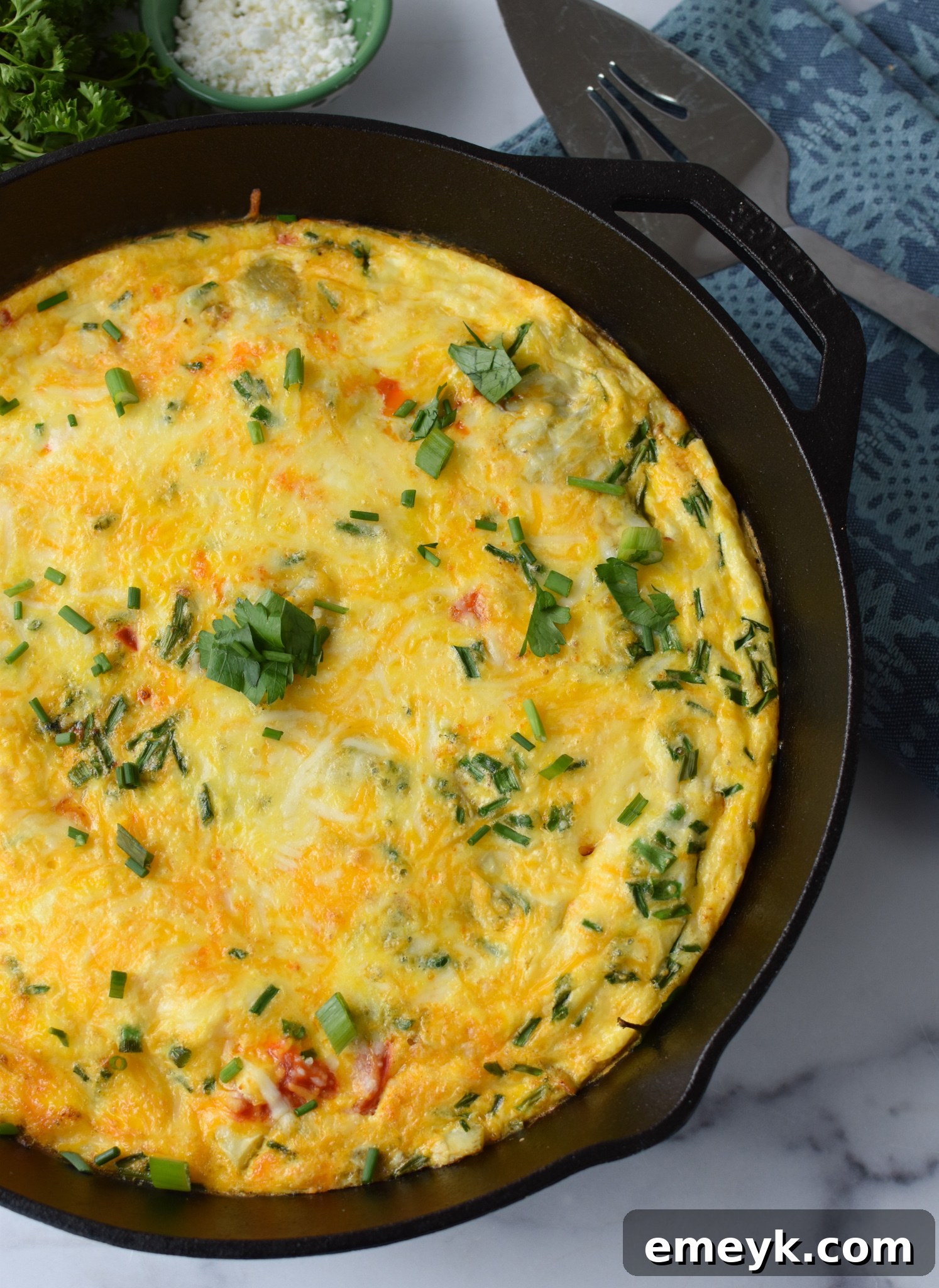 A whole Mediterranean Vegetable Frittata garnished with fresh parsley on a wooden board.