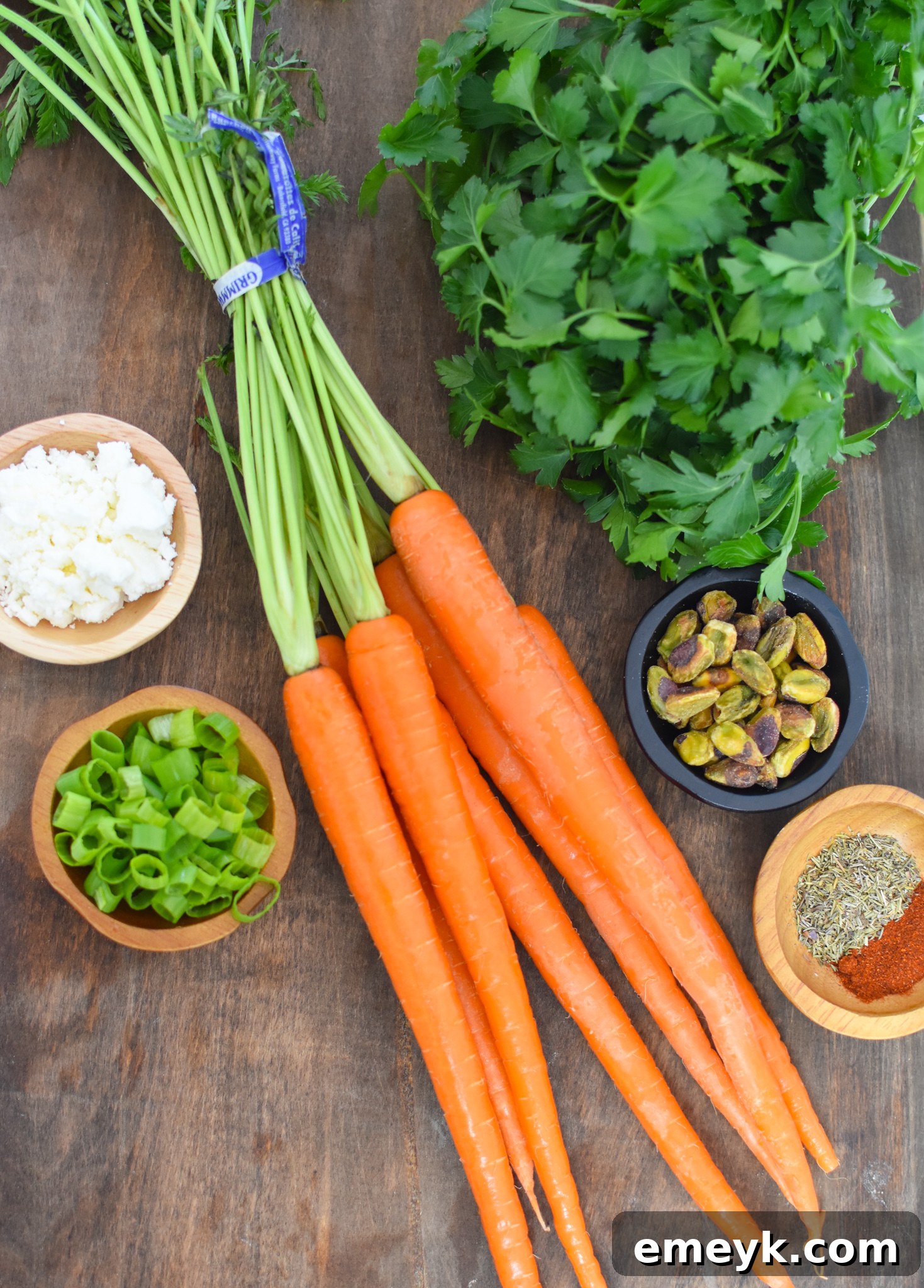 A flat lay photograph showcasing all the fresh ingredients needed for Roasted Carrots with Pistachios, including whole carrots, herbs, feta, and pistachios.