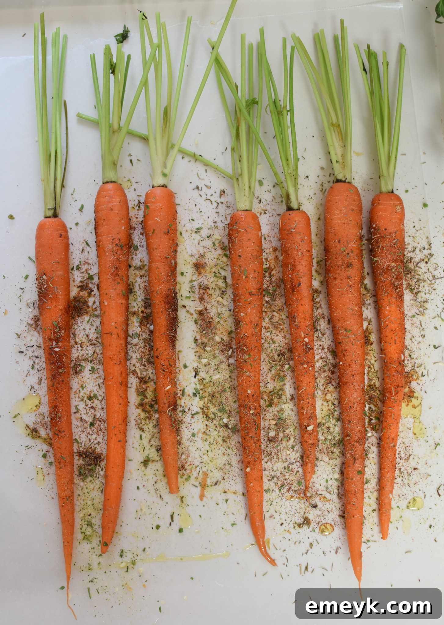 Raw carrots coated in spices and olive oil, spread out on a parchment-lined baking sheet, ready for roasting.