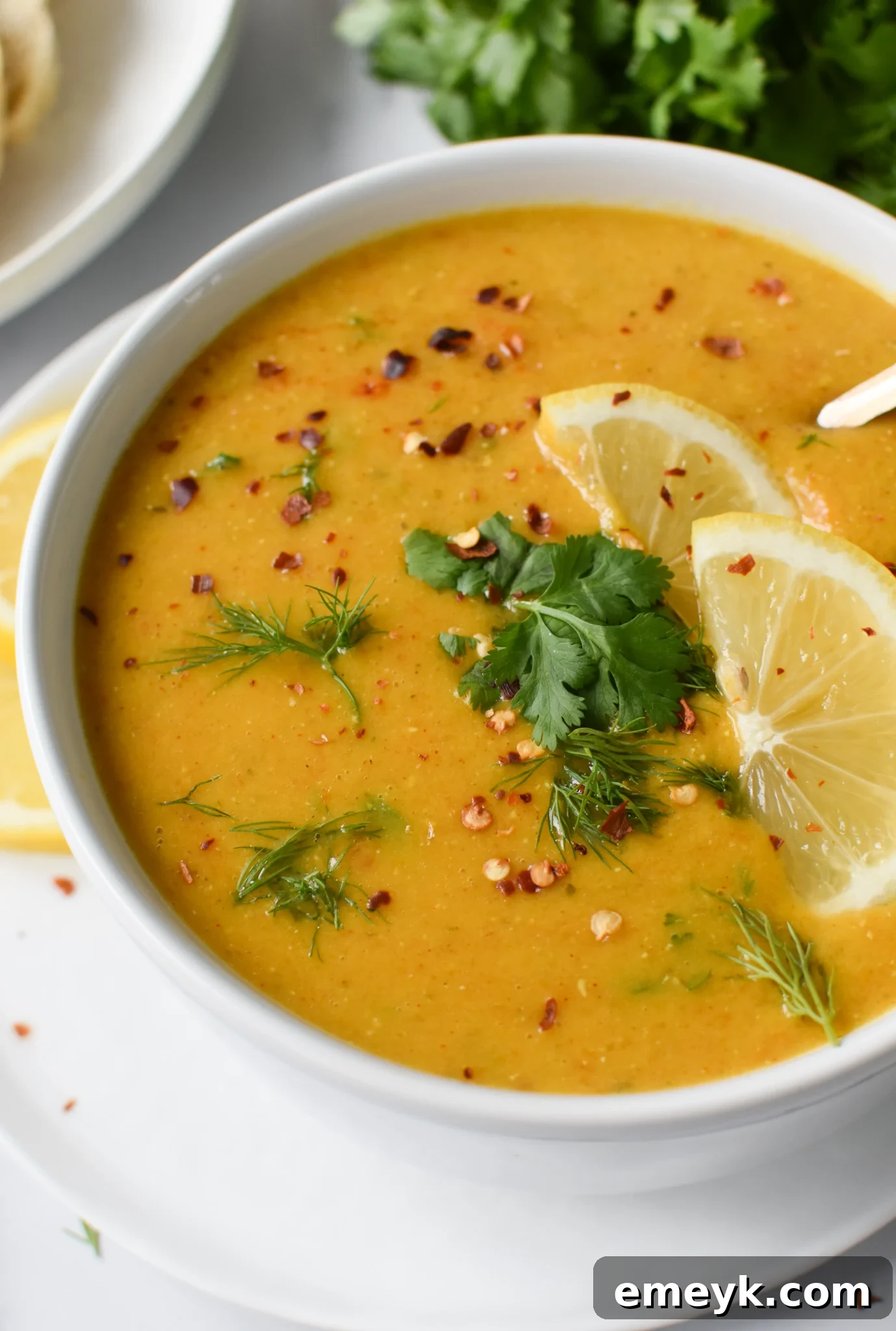 A steaming bowl of Lemon Lentil Soup garnished with fresh lemon wedges and herbs.
