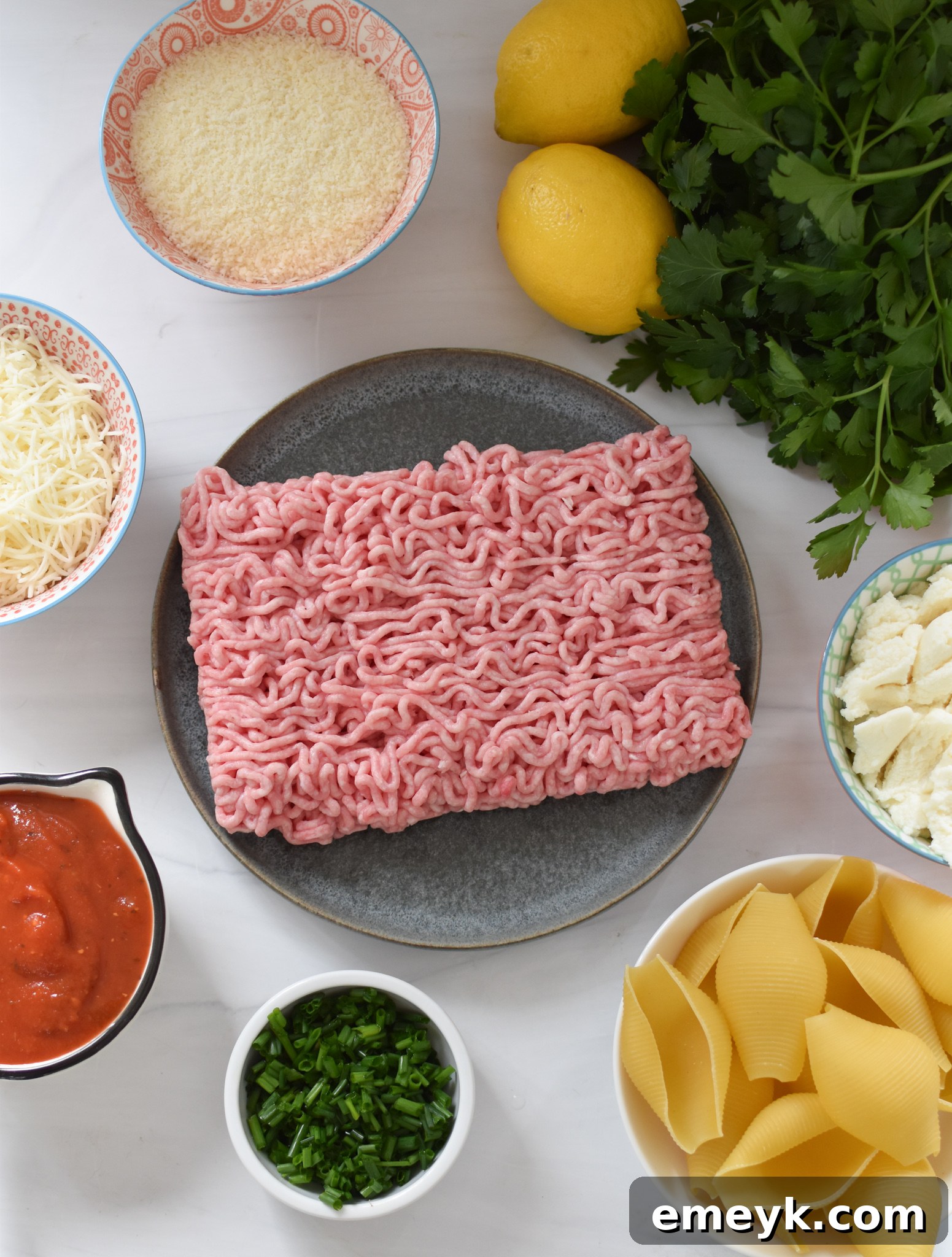 An array of fresh ingredients for Veal Stuffed Shells including ground veal, cheeses, tomatoes, herbs, and lemon.