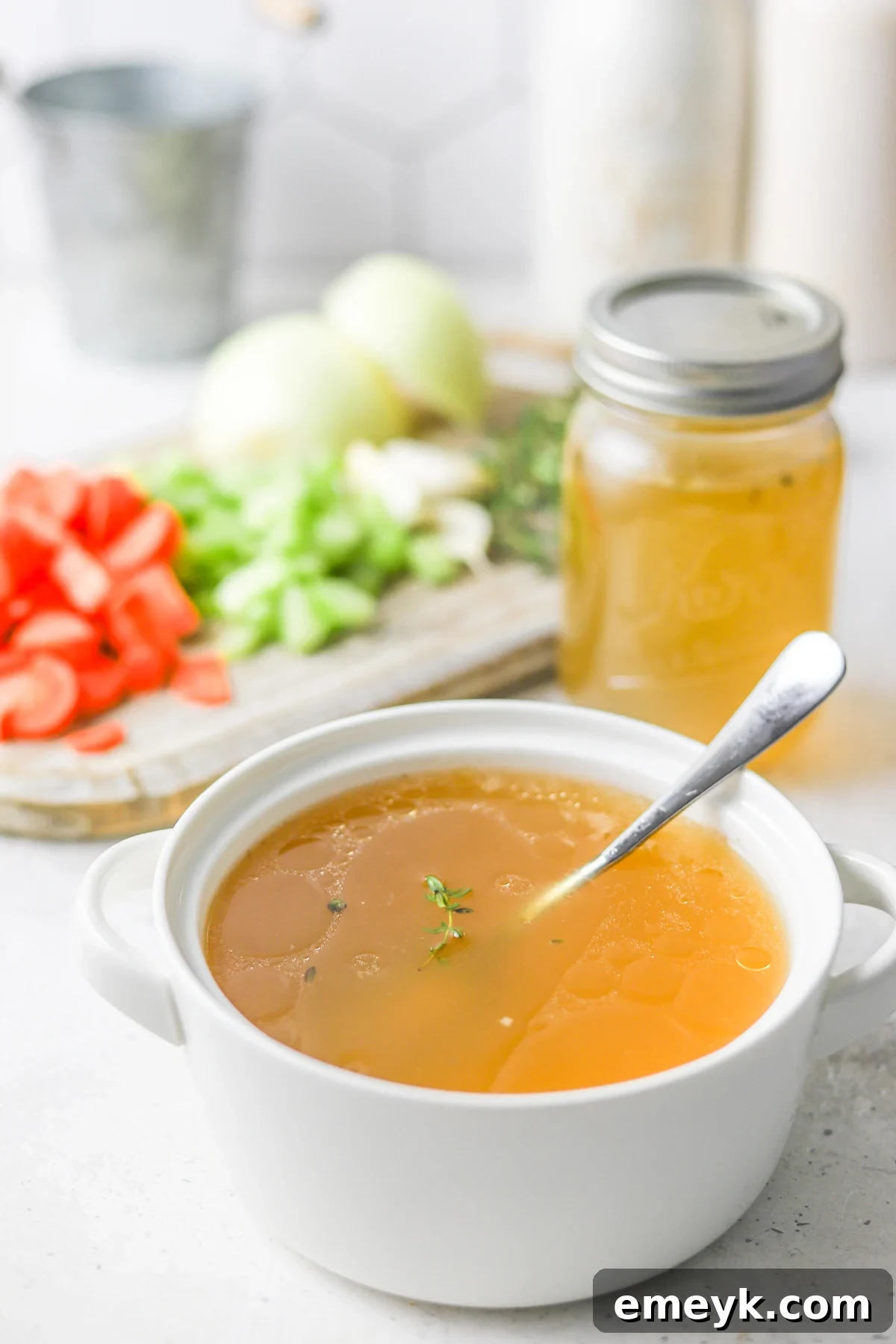 A ladle of rich, golden homemade chicken broth being poured into a bowl.