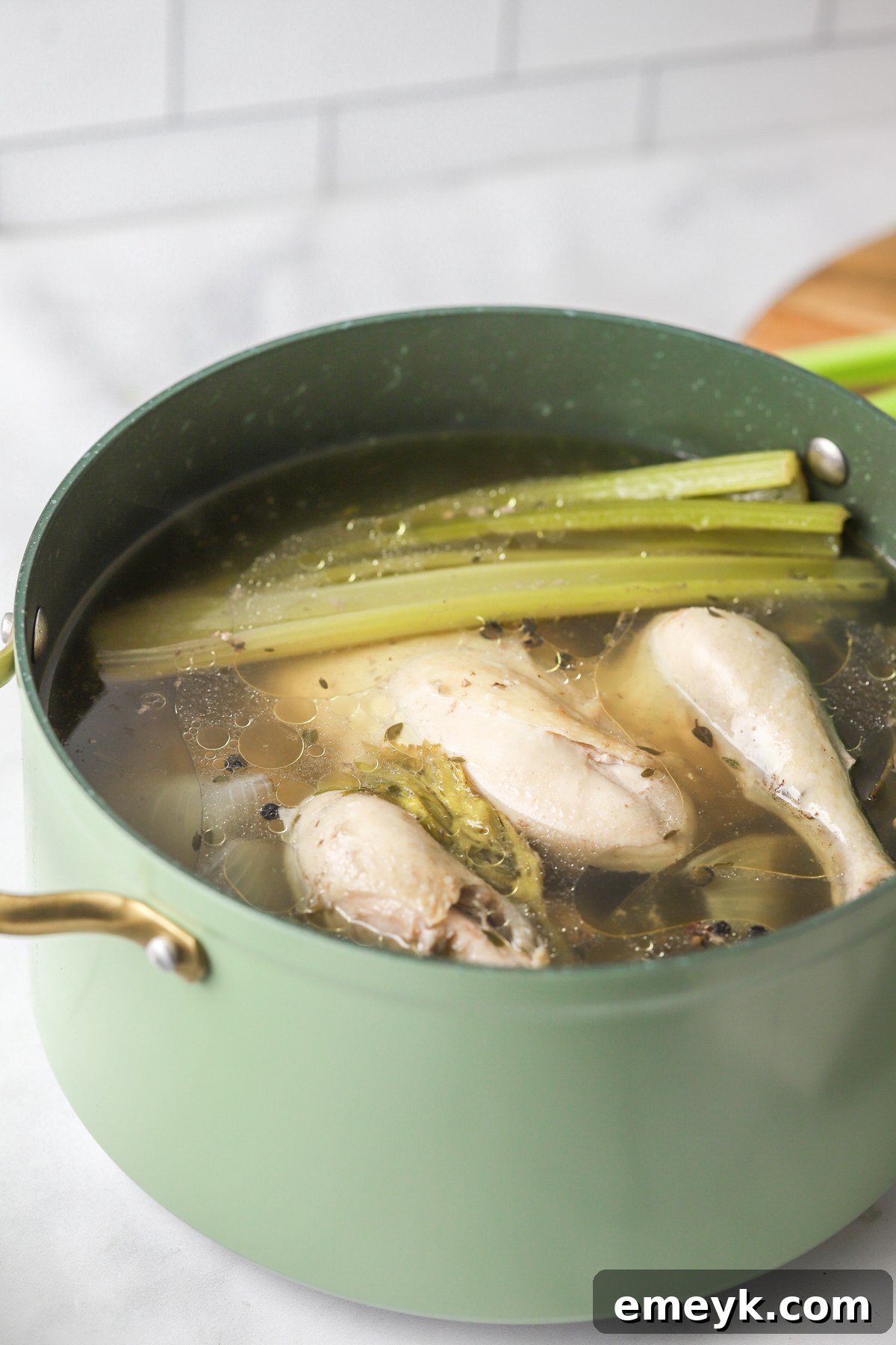 Chicken, vegetables, and herbs simmering in water in a large pot.