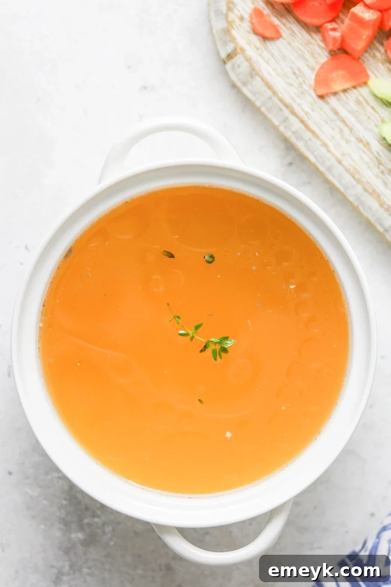 A beautiful, clear bowl of homemade chicken broth with fresh herbs.