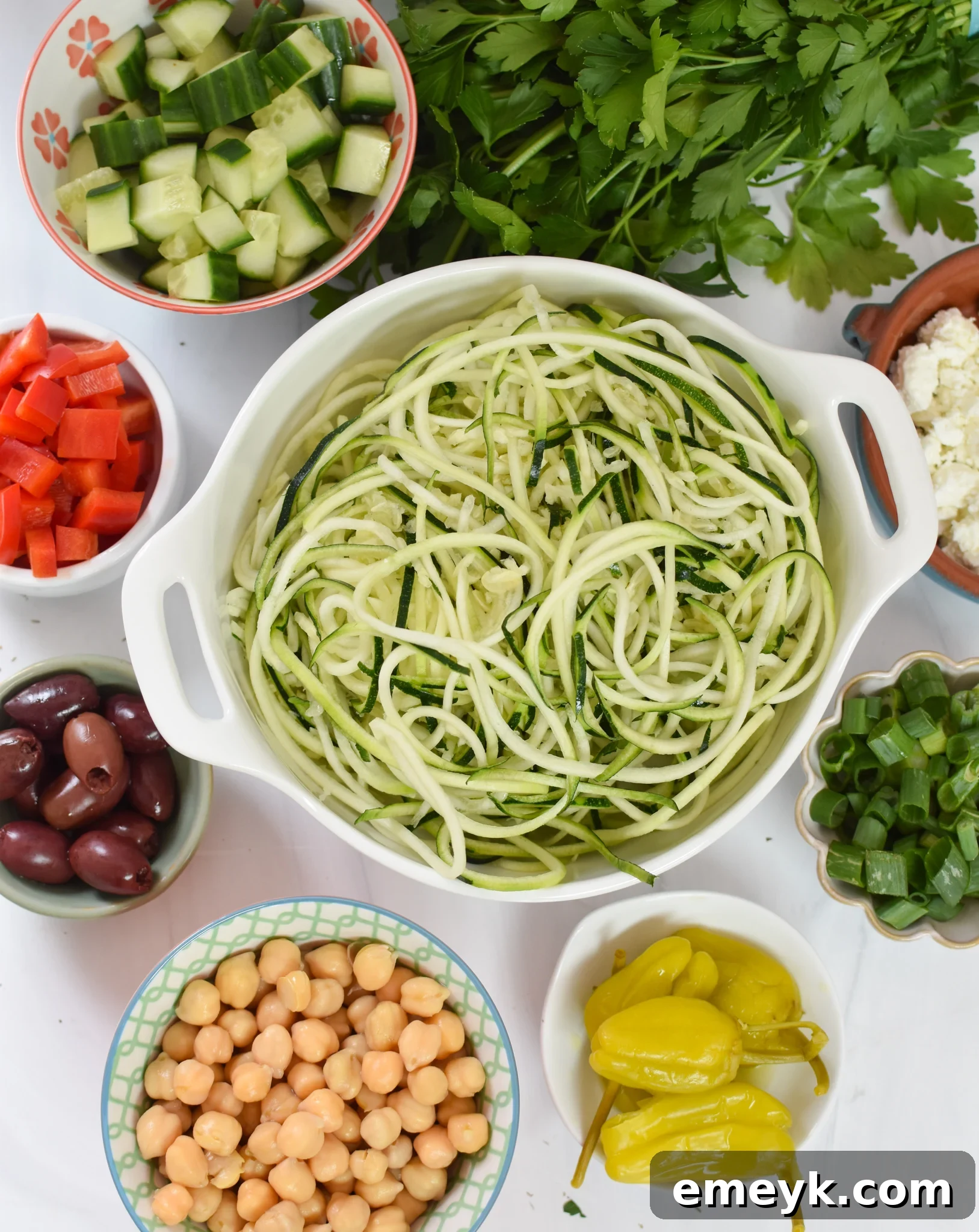 Zucchini and Pasta Mediterranean Medley 3 A collection of fresh ingredients for Mediterranean Zucchini Pasta Salad, including zucchini, chickpeas, cucumbers, tomatoes, bell peppers, olives, and feta cheese.