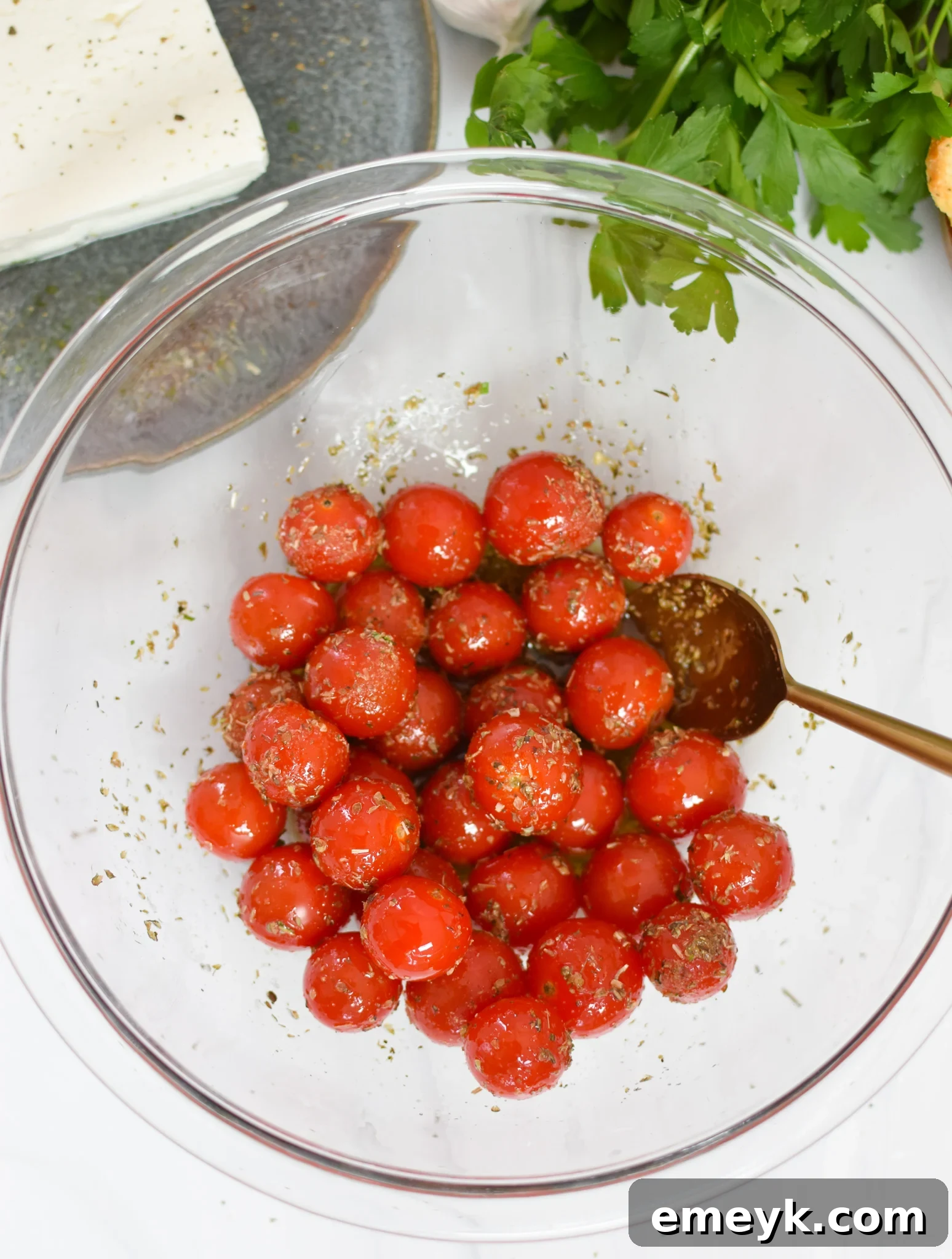 Effortless Baked Feta Delight 5 Cherry tomatoes coated in olive oil in a mixing bowl for baked feta.