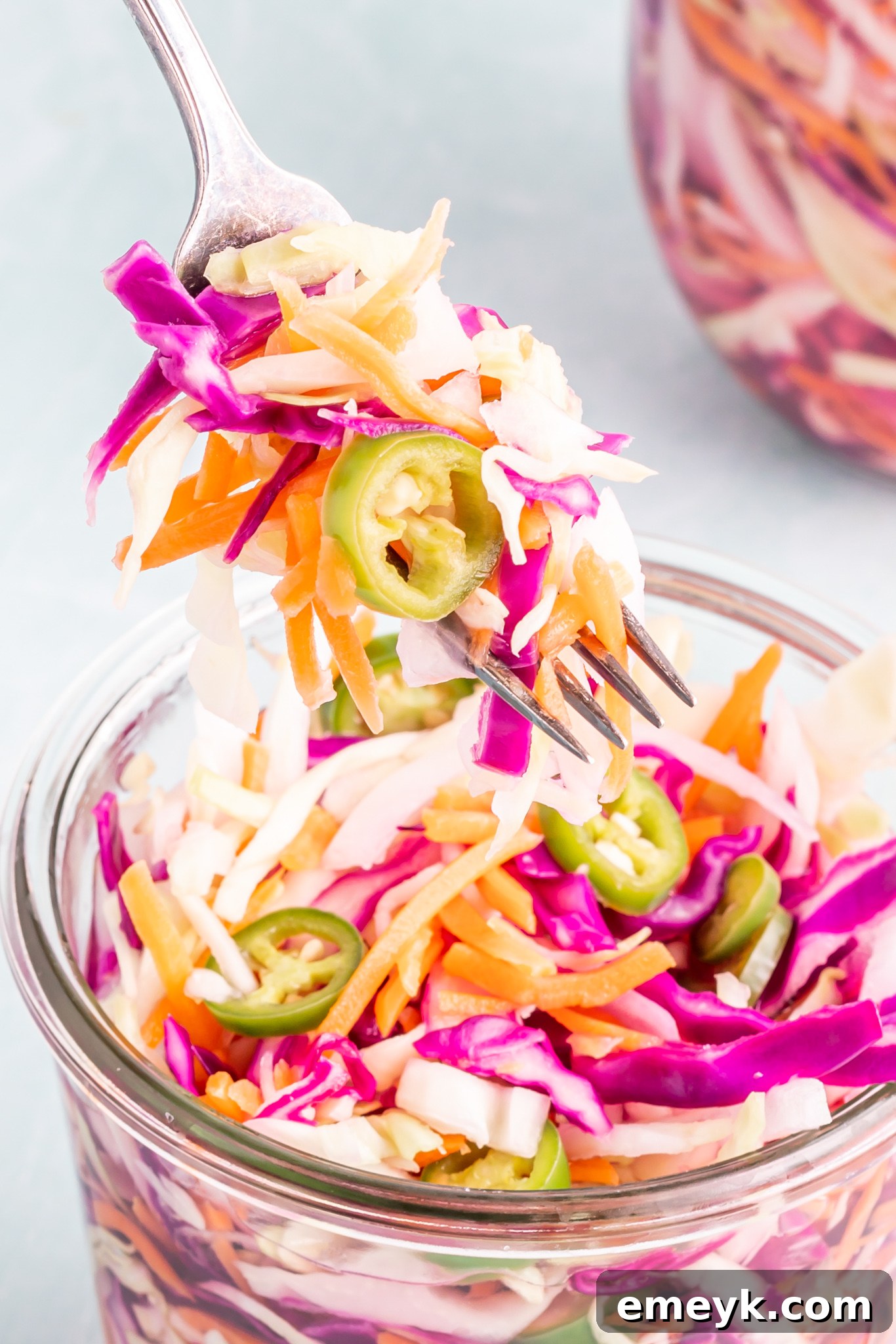 Easy Curtido Recipe served in a clear glass jar with a fork ready to be enjoyed as a fresh condiment.