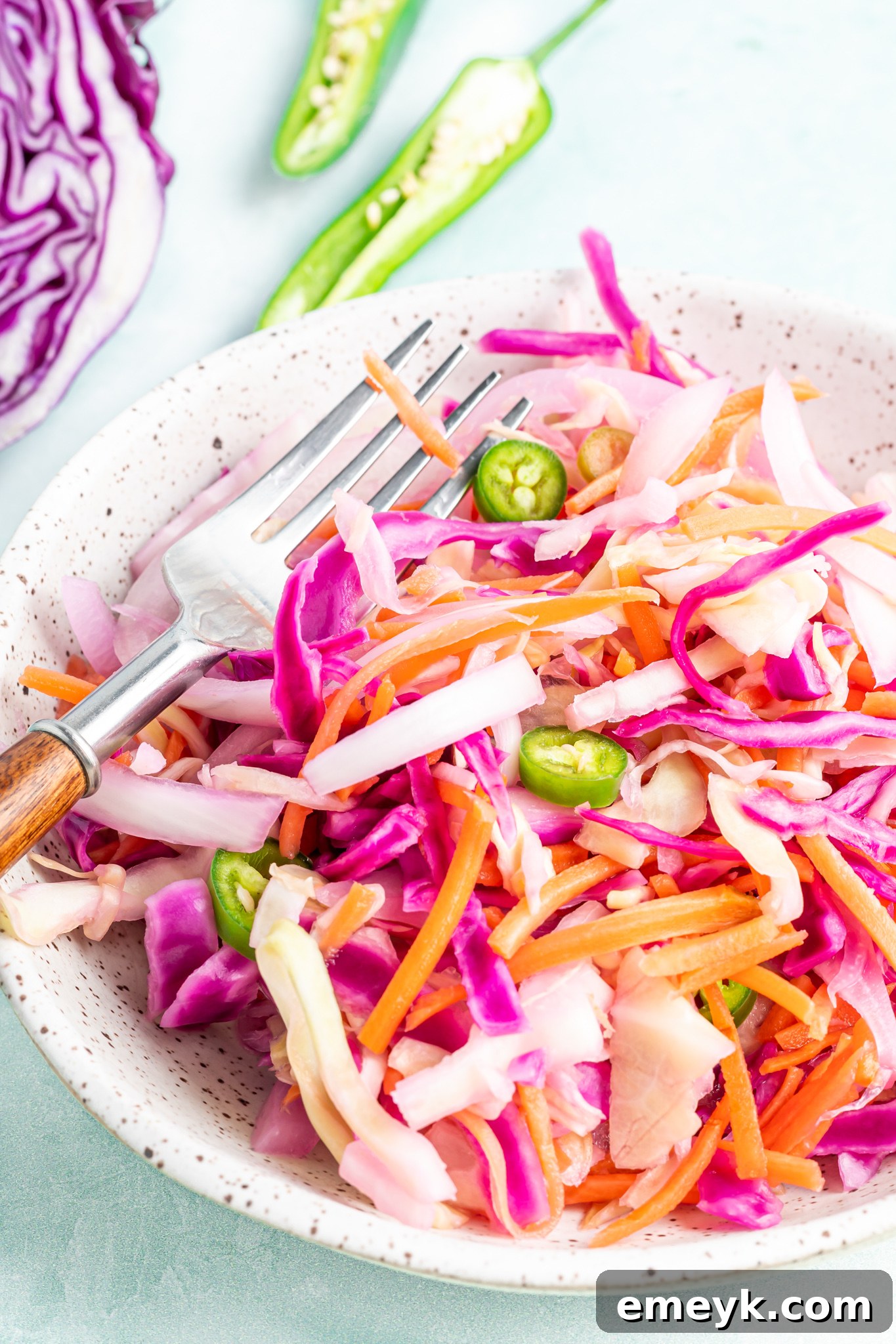 A large mixing bowl filled with colorful shredded vegetables and thinly sliced jalapeños for Curtido preparation.