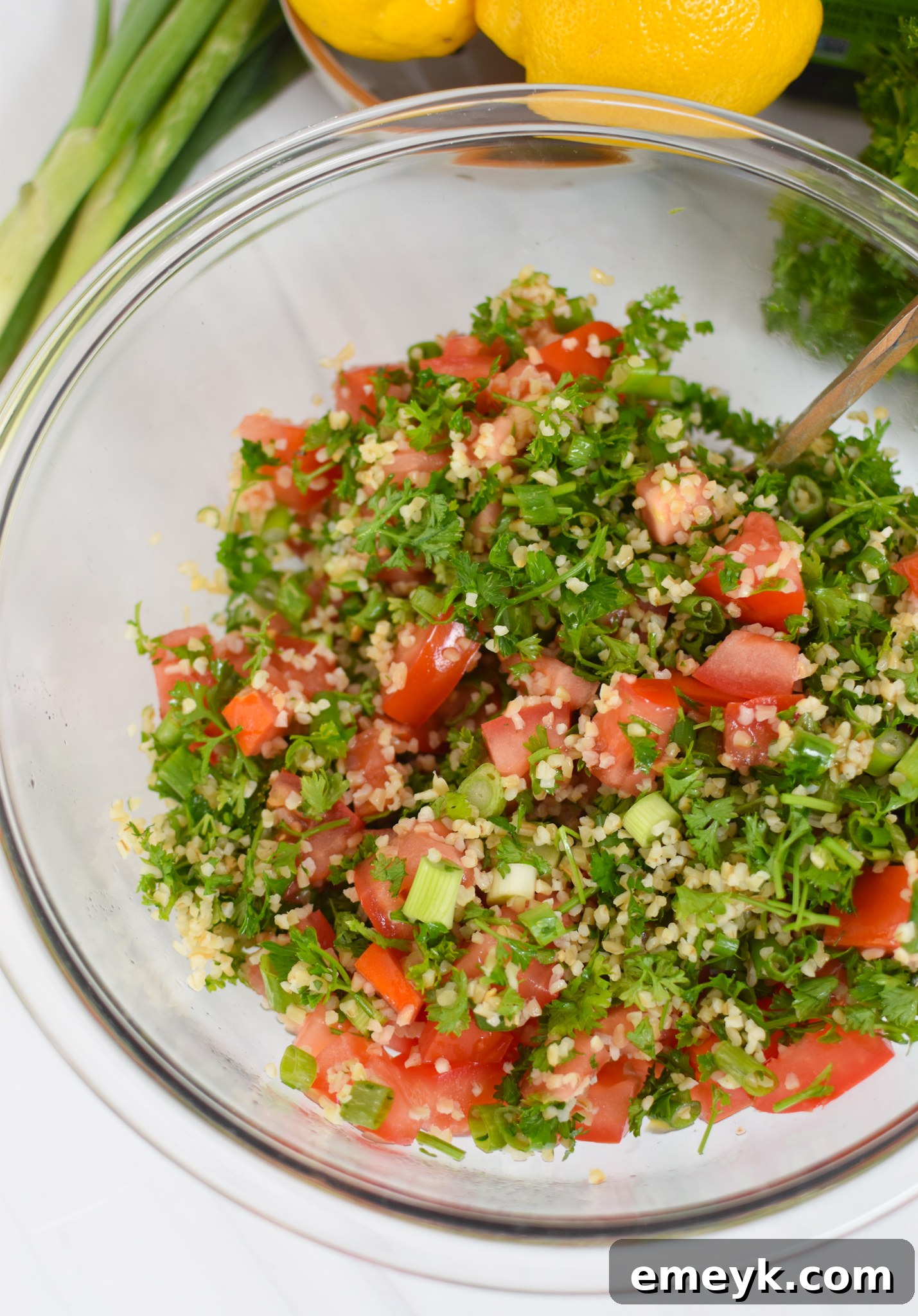 Close-up of freshly mixed tabbouleh, showing fine bulgur, chopped parsley, tomatoes, green onions, and mint.