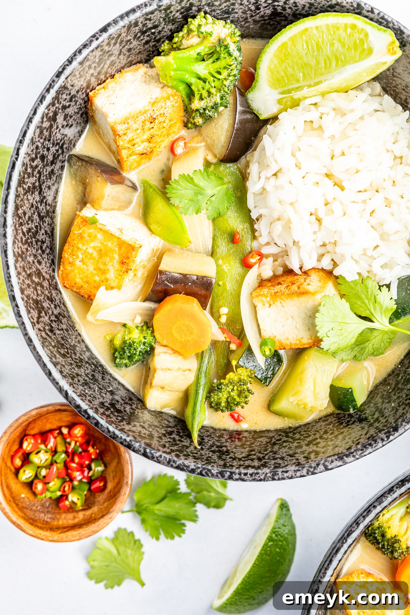 A vibrant bowl of Thai Vegetable Green Curry, rich with green sauce, colorful vegetables, and tofu chunks, garnished with cilantro.