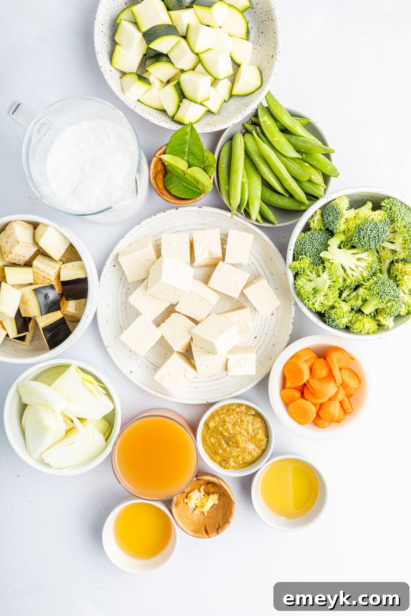Assorted fresh ingredients for Thai Vegetable Green Curry, including tofu, vegetables, curry paste, and lime leaves, neatly arranged on a cutting board.