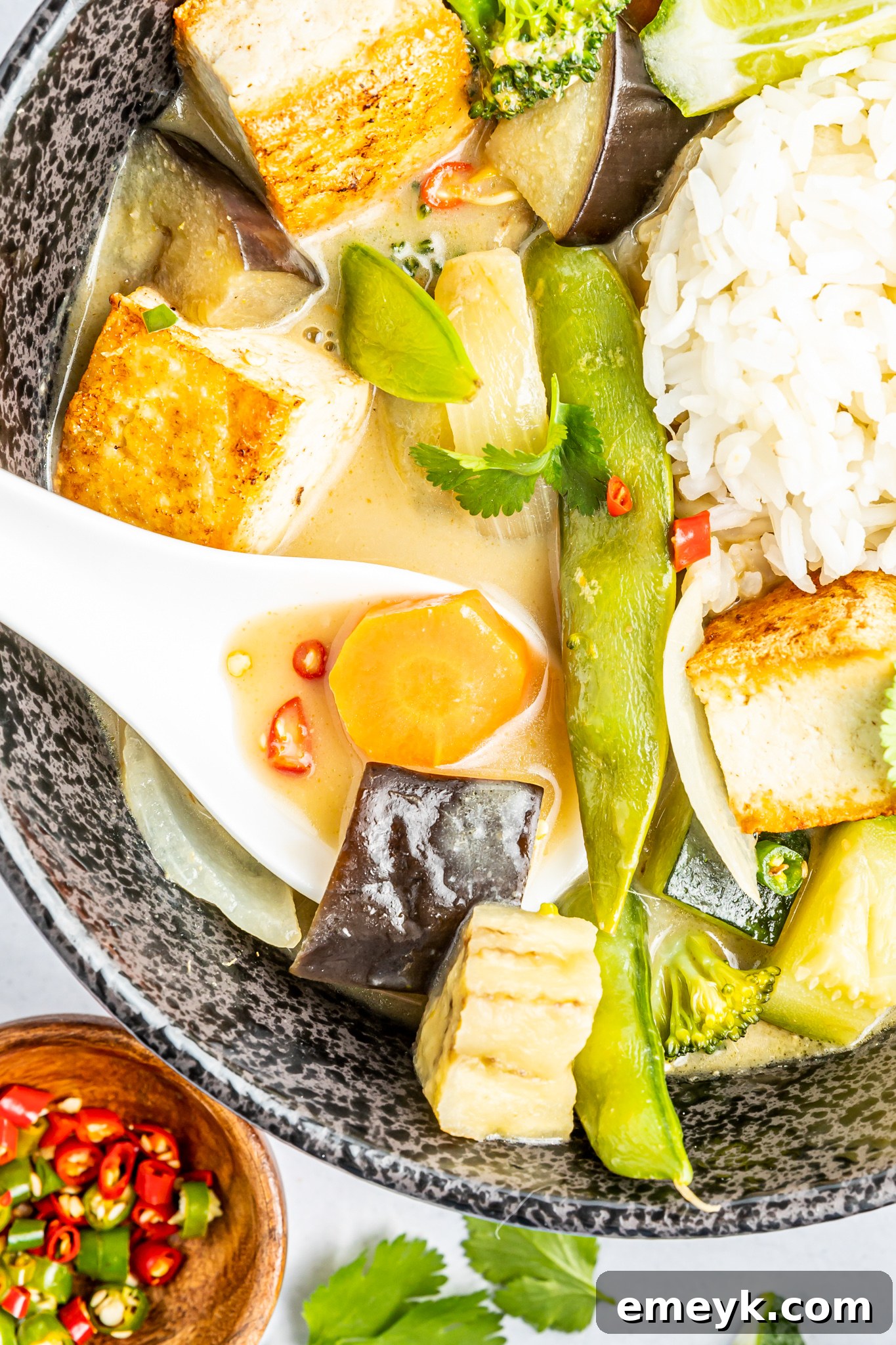 A serving of Thai Vegetable Green Curry in a gray bowl, with a spoon resting inside, showcasing its creamy texture and visible vegetable pieces.