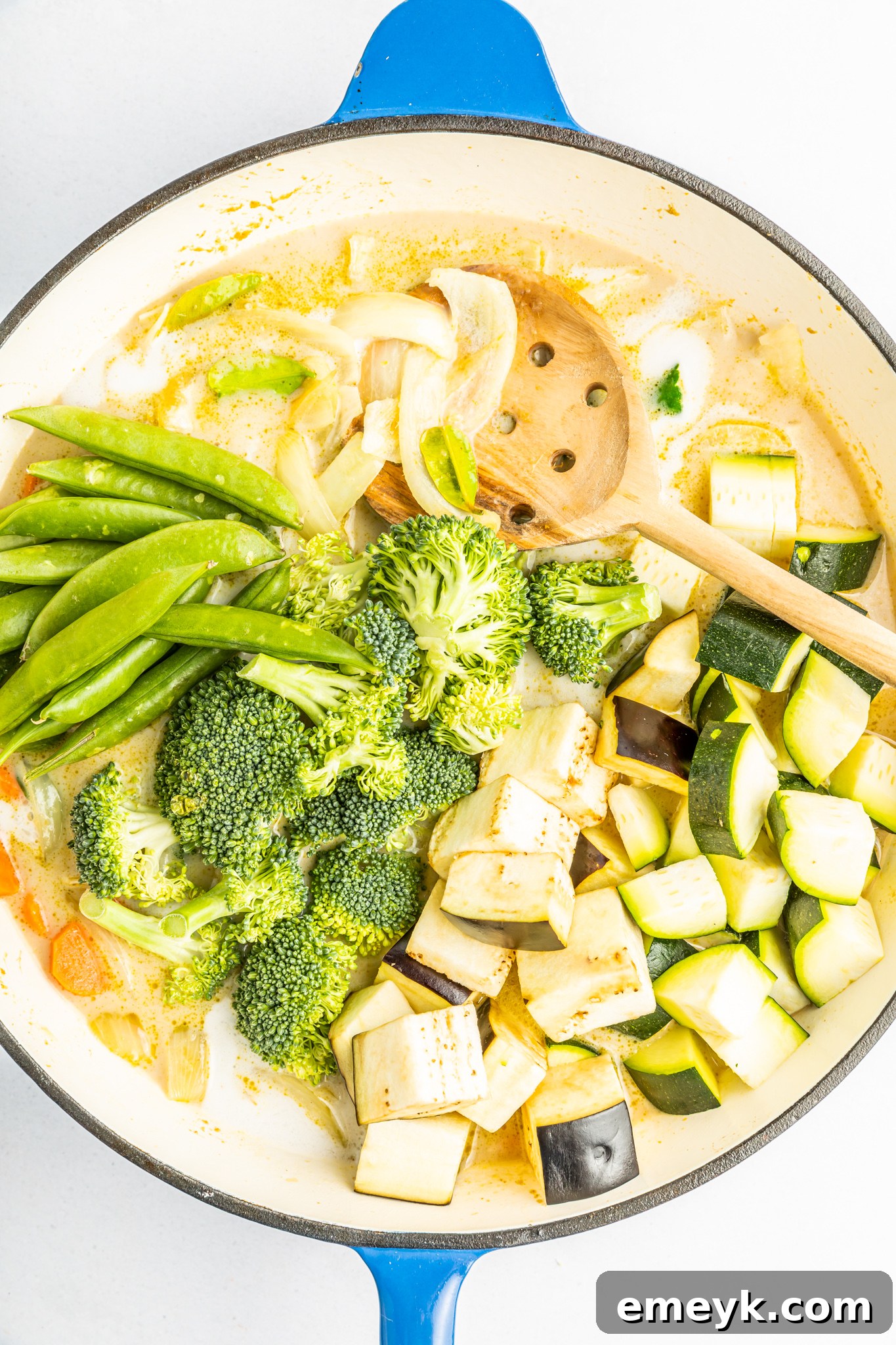 Thai Green Curry paste being stirred into sautéed vegetables in a pot, creating the rich base for the curry sauce.
