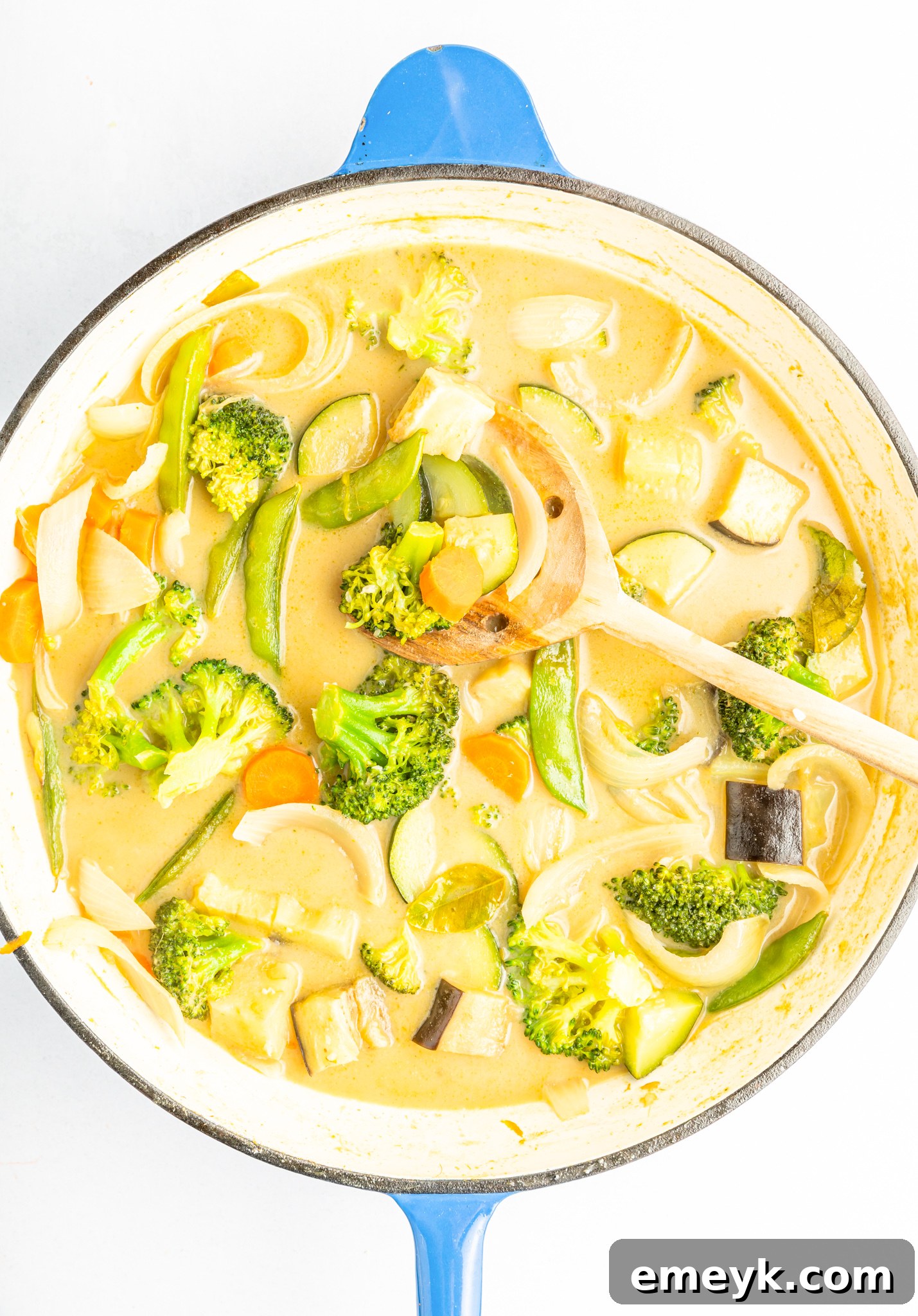 A ladle serving a bowl of Thai Vegetable Green Curry, showing the rich green sauce, diverse vegetables, and tofu pieces, ready to be enjoyed.