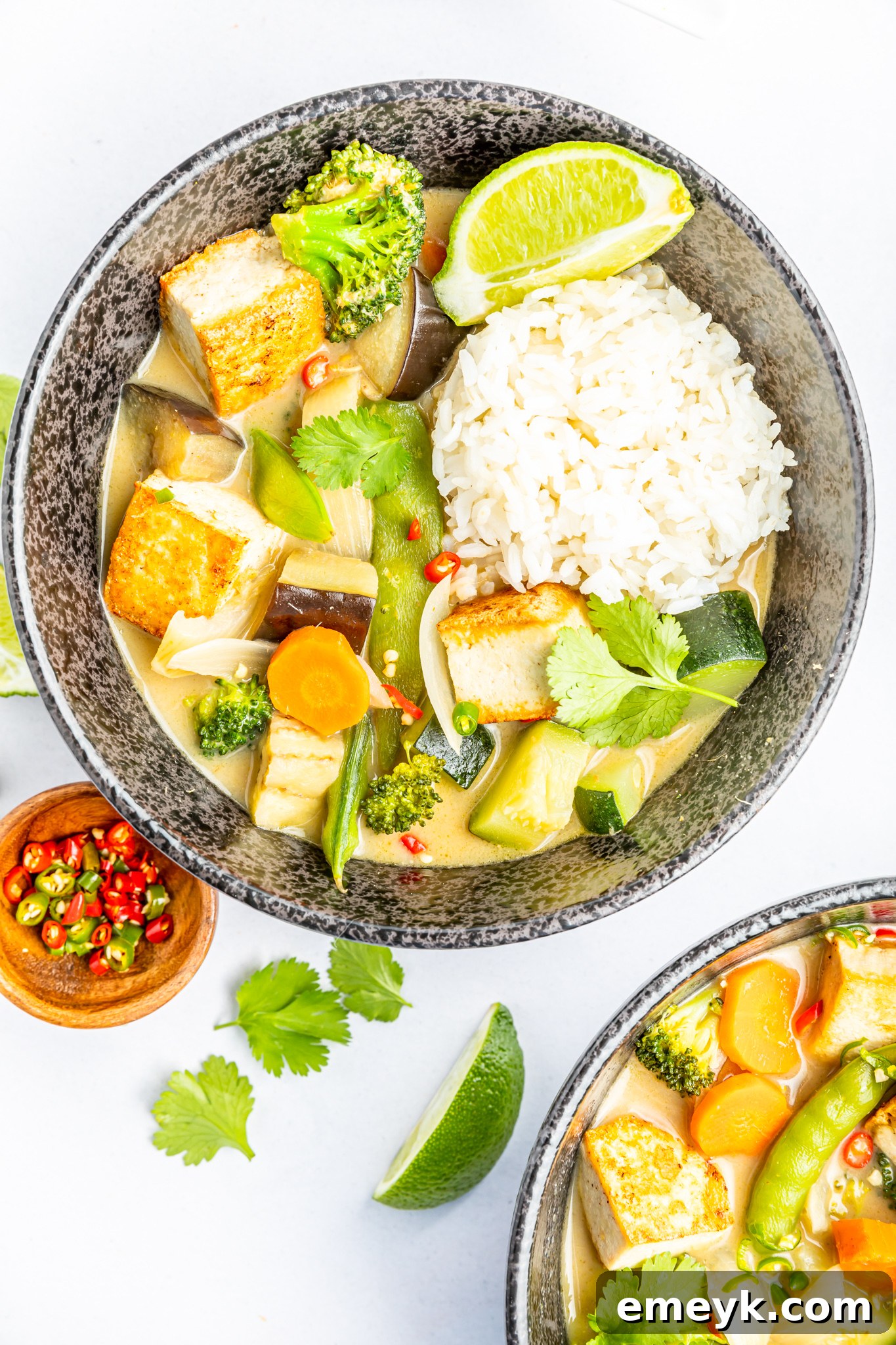 A bowl of Thai Vegetable Green Curry served with a side of steamed white rice, garnished with fresh cilantro, ready for a delicious meal.