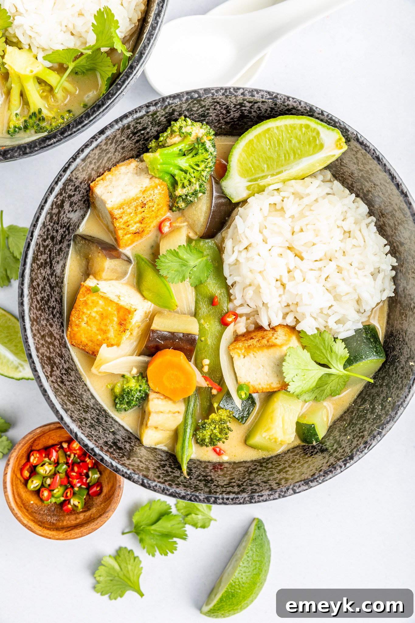 A bowl of Thai Vegetable Green Curry garnished with fresh lime wedges, emphasizing its fresh and zesty flavors.