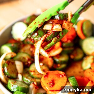 Quick Korean Cucumber Kimchi with tongs, lifting a portion from a white bowl, inviting to be tasted.