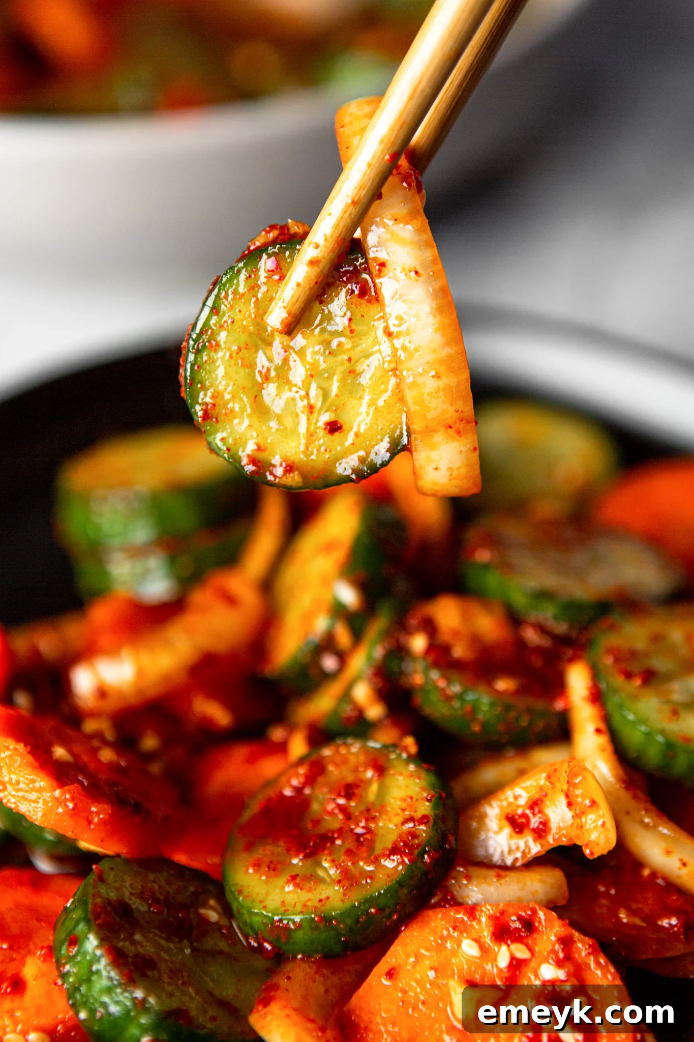 Quick Korean Cucumber Kimchi in a bowl, with chopsticks poised to pick up a slice, emphasizing its immediate readiness and appeal.