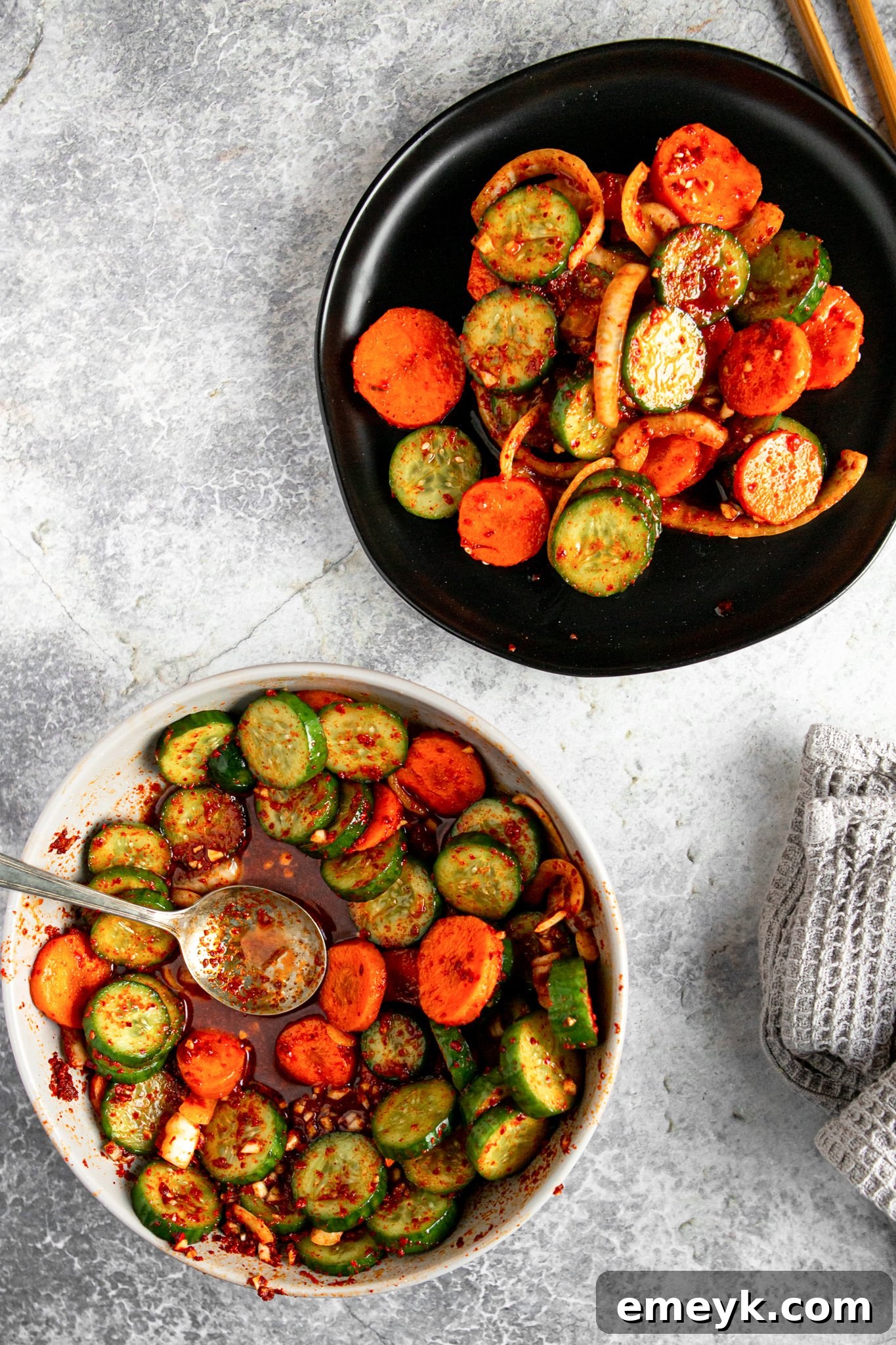 A pristine white bowl filled with freshly made Quick Korean Cucumber Kimchi, ready to be served. The bright red sauce beautifully coats the green cucumbers and orange carrots.