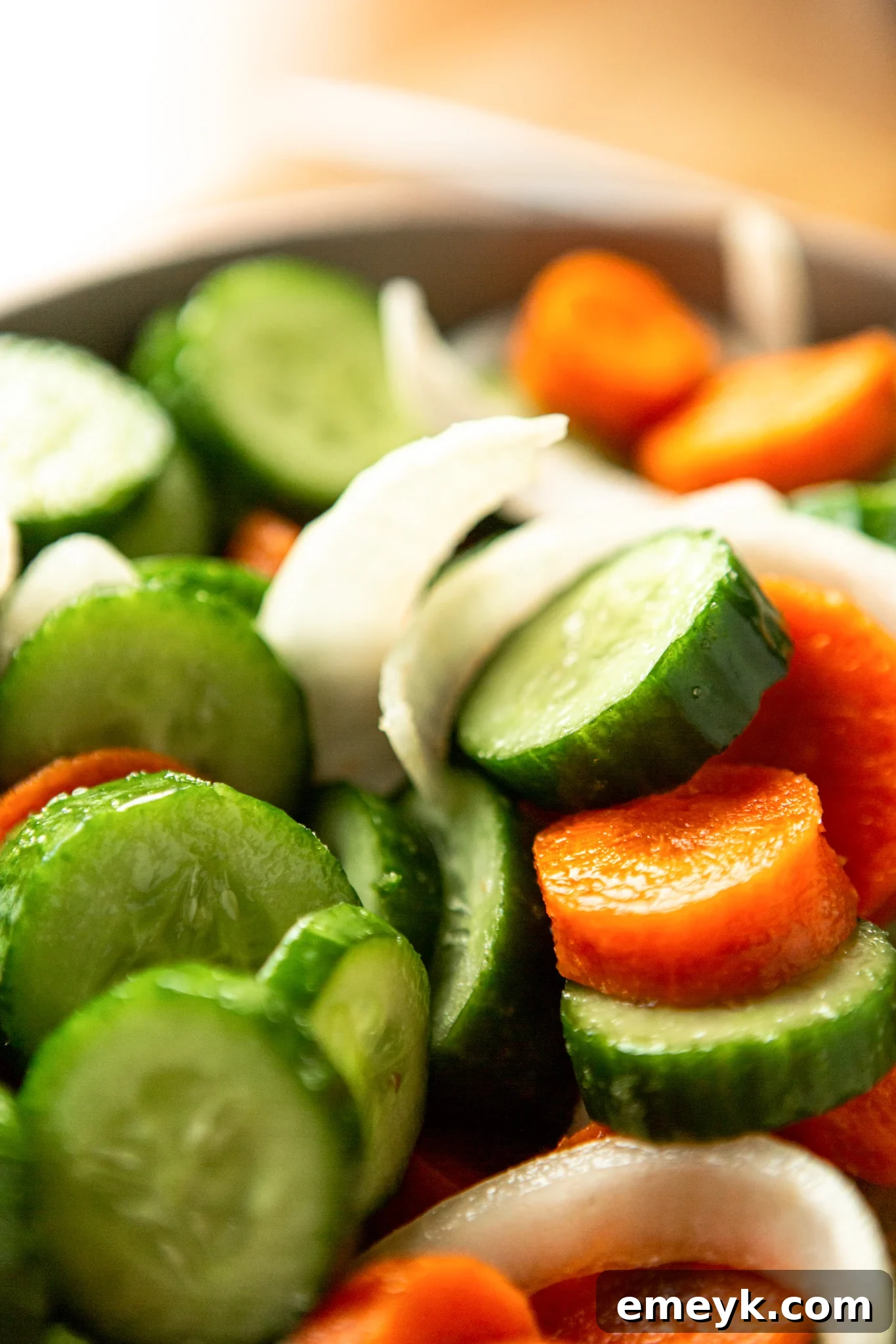 A bowl of sliced cucumbers, carrots, and onions, having just been salted, with visible moisture beginning to release, preparing for the kimchi process.