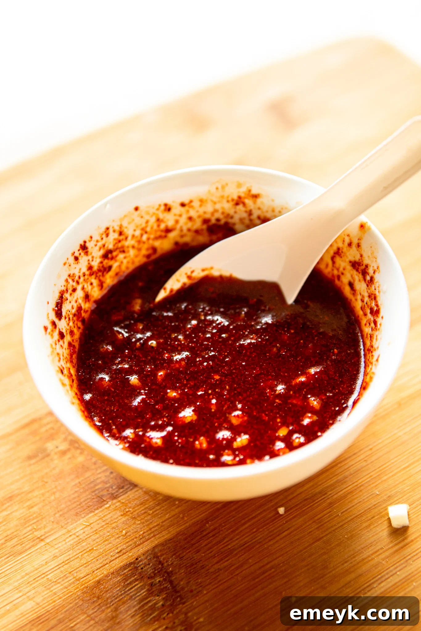 A small bowl containing the vibrant Korean red chili pepper powder, rice vinegar, soy sauce, sesame oil, and sugar, thoroughly mixed into the kimchi seasoning sauce.