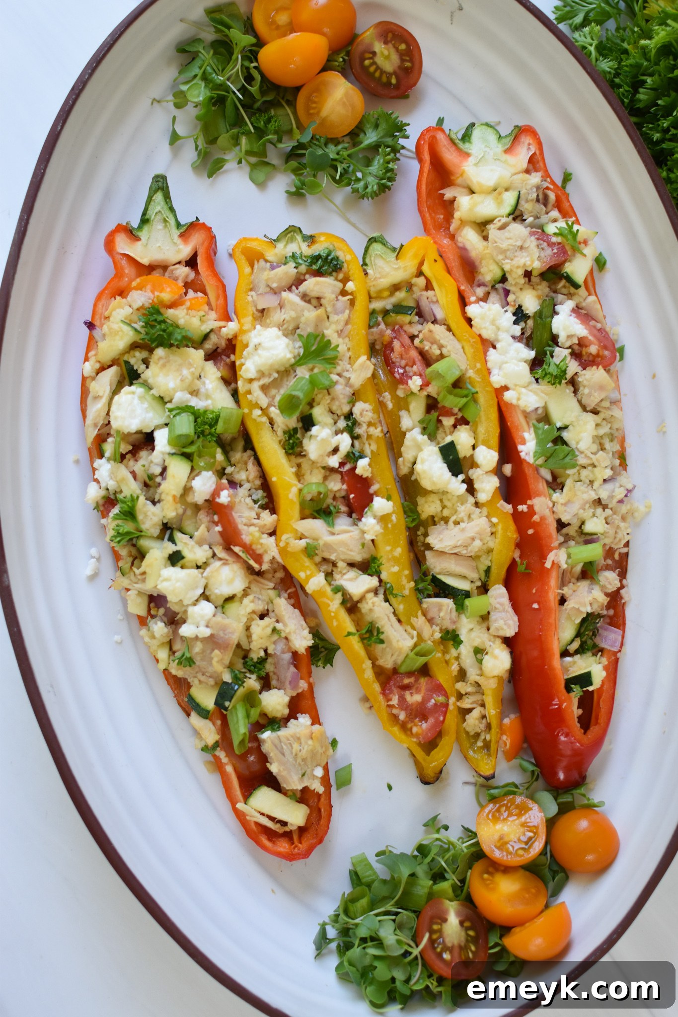 Mediterranean Tuna Couscous Stuffed Peppers on a white platter, garnished with fresh herbs.