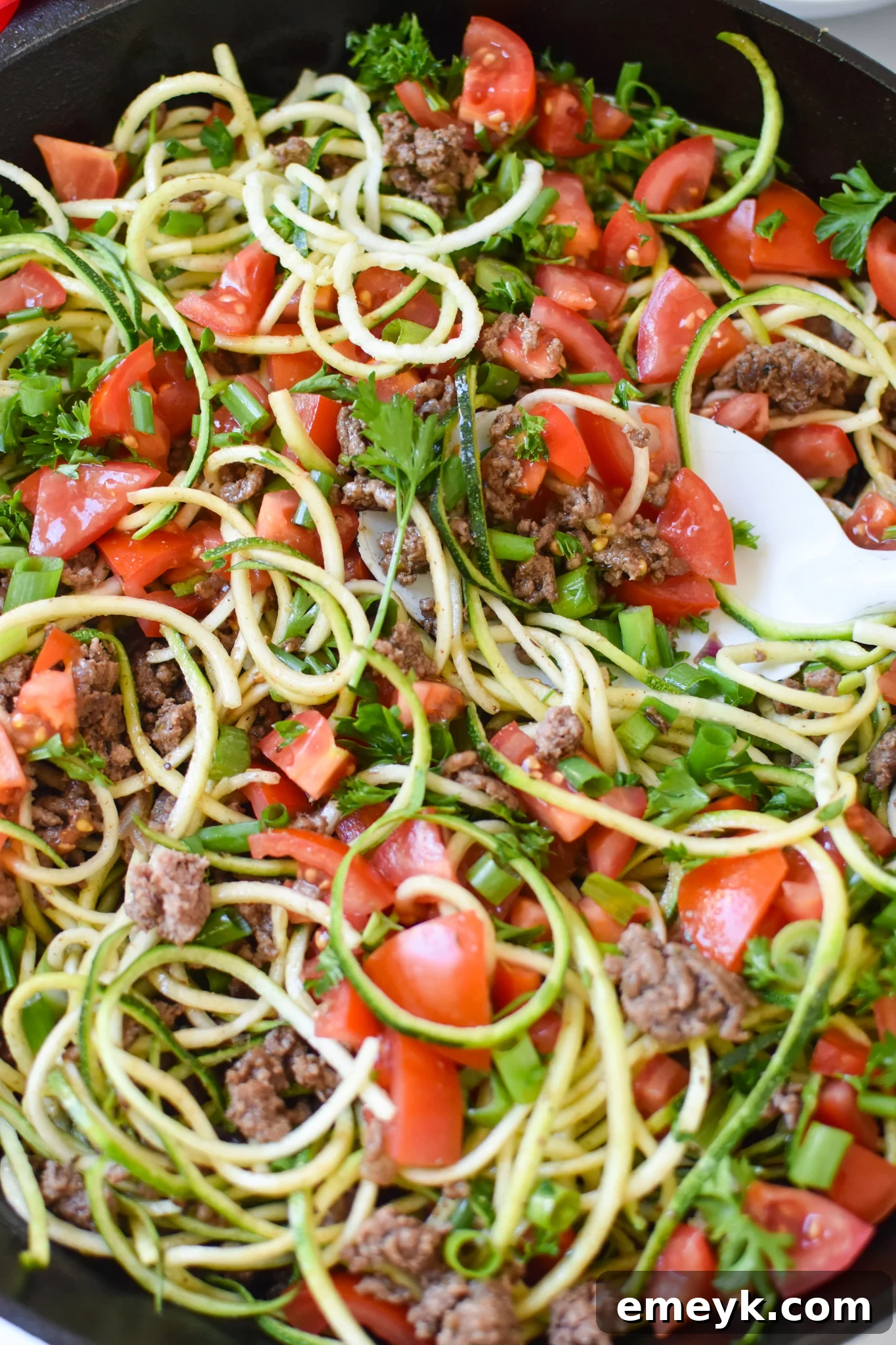 Close-up of a serving of Mediterranean Ground Beef Zucchini Skillet with a white serving spoon, showing the rich texture and fresh ingredients.