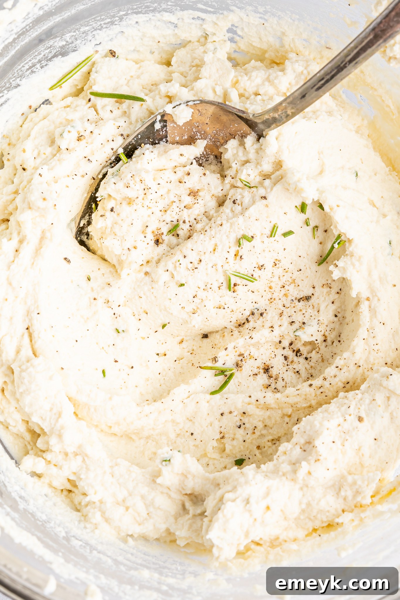 Polenta rounds in a bowl, coated with olive oil and rosemary before roasting.
