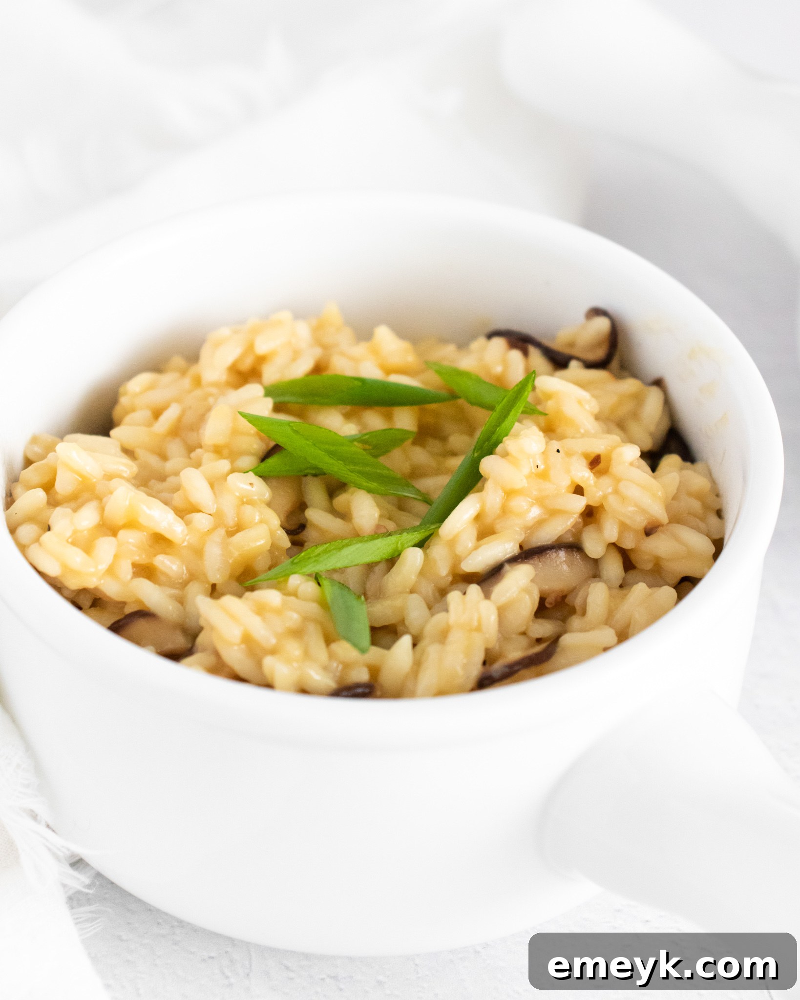 A bowl of Instant Pot Mushroom Risotto topped with green onions and a lemon wedge.