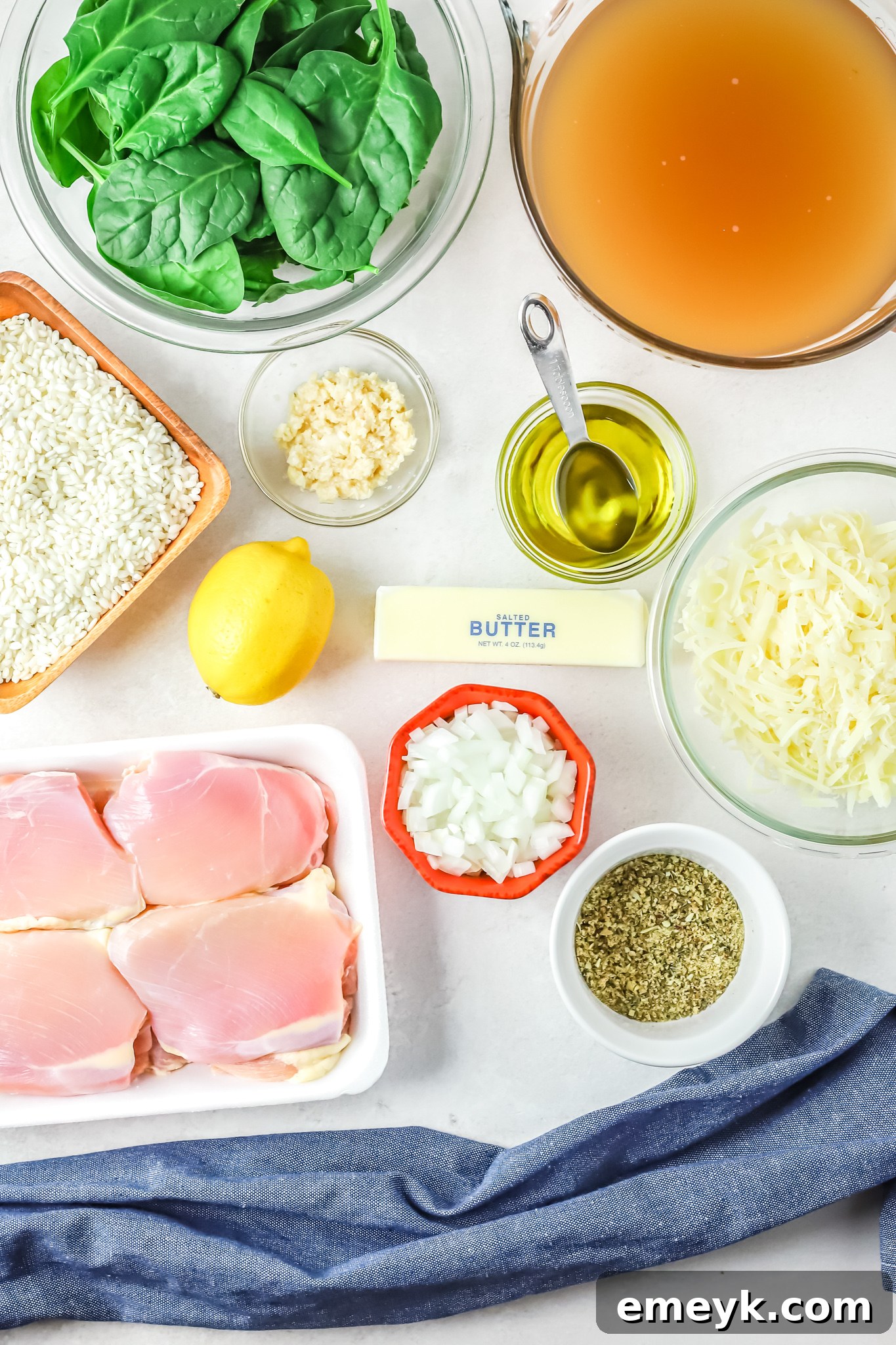 Various ingredients for Oven Baked Chicken Thighs with Risotto laid out on a wooden surface, including chicken, rice, spinach, and spices.
