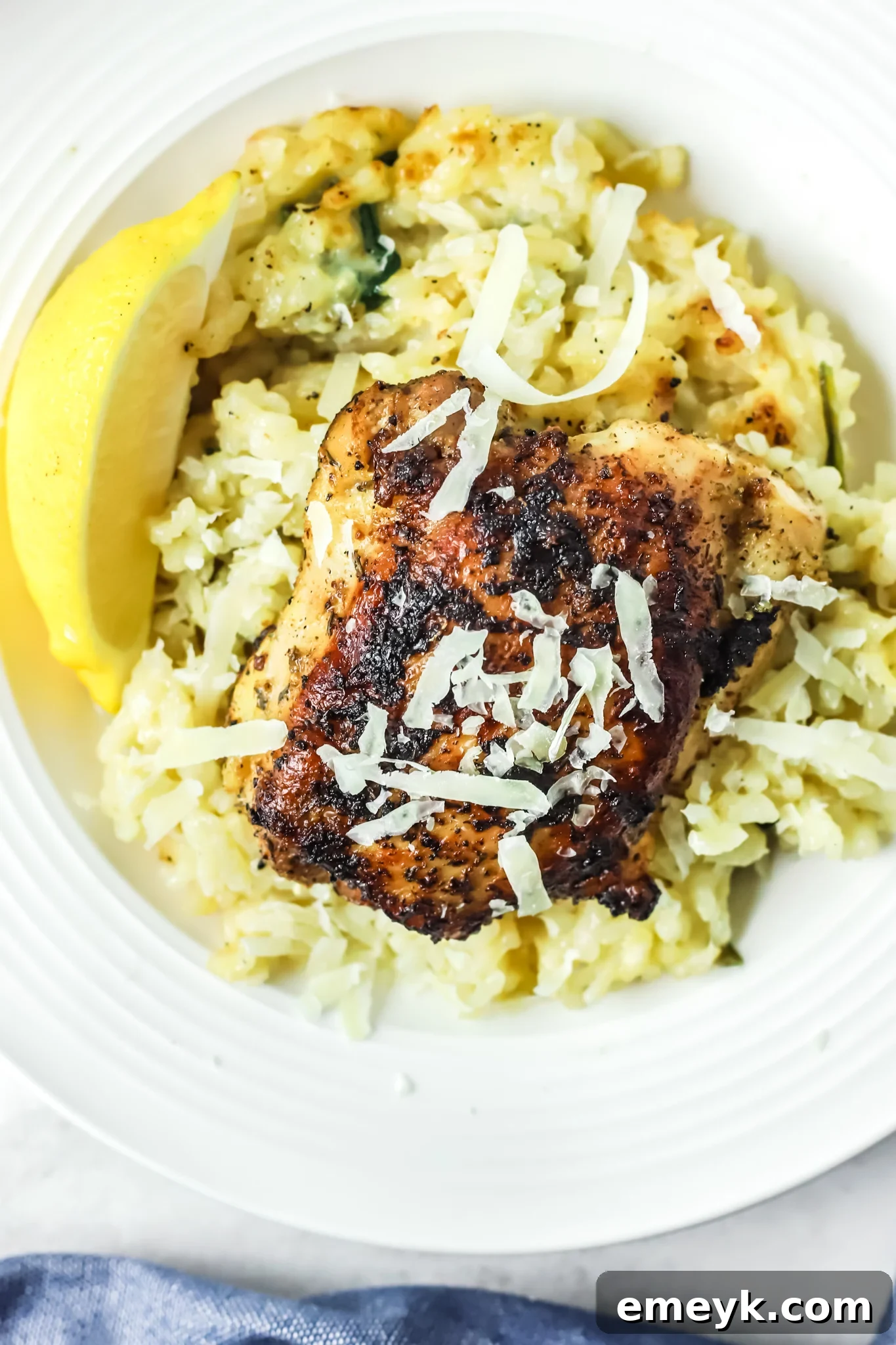 Oven Baked Chicken Thighs with Risotto, focusing on the creamy texture of the risotto and a generous sprinkle of Parmesan cheese.