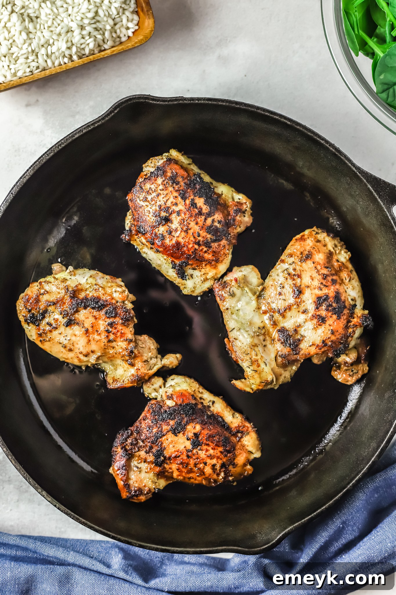 Searing seasoned chicken thighs in a hot skillet, a step in making Oven Baked Chicken Thighs with Risotto.
