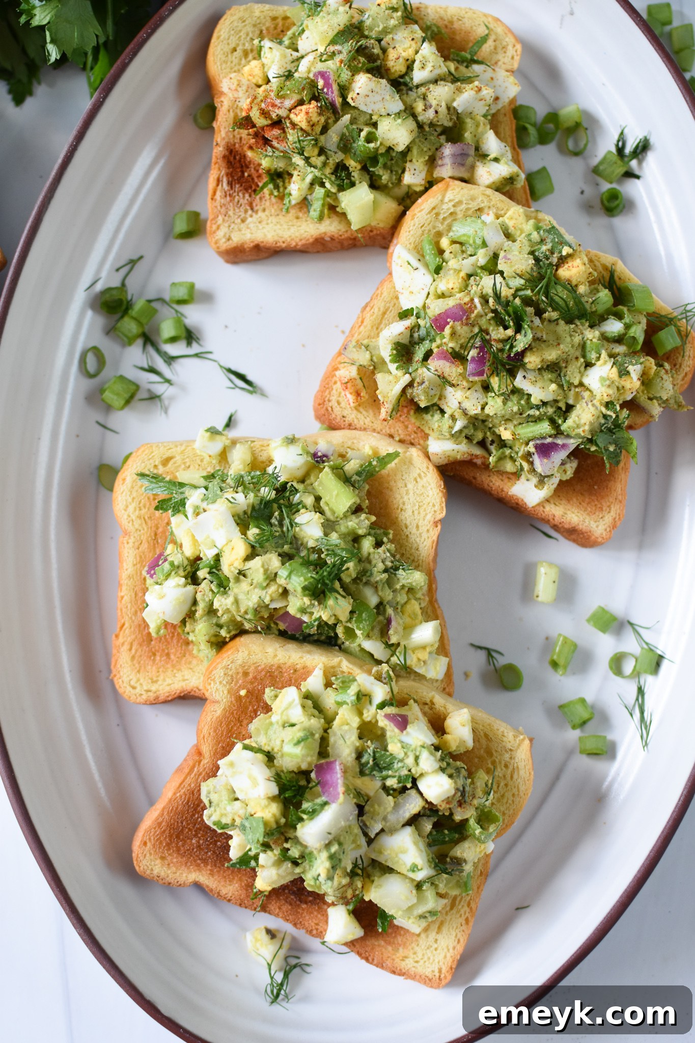 Avocado Egg Salad generously piled on perfectly golden-brown toasted brioche bread, artfully arranged on a serving platter.