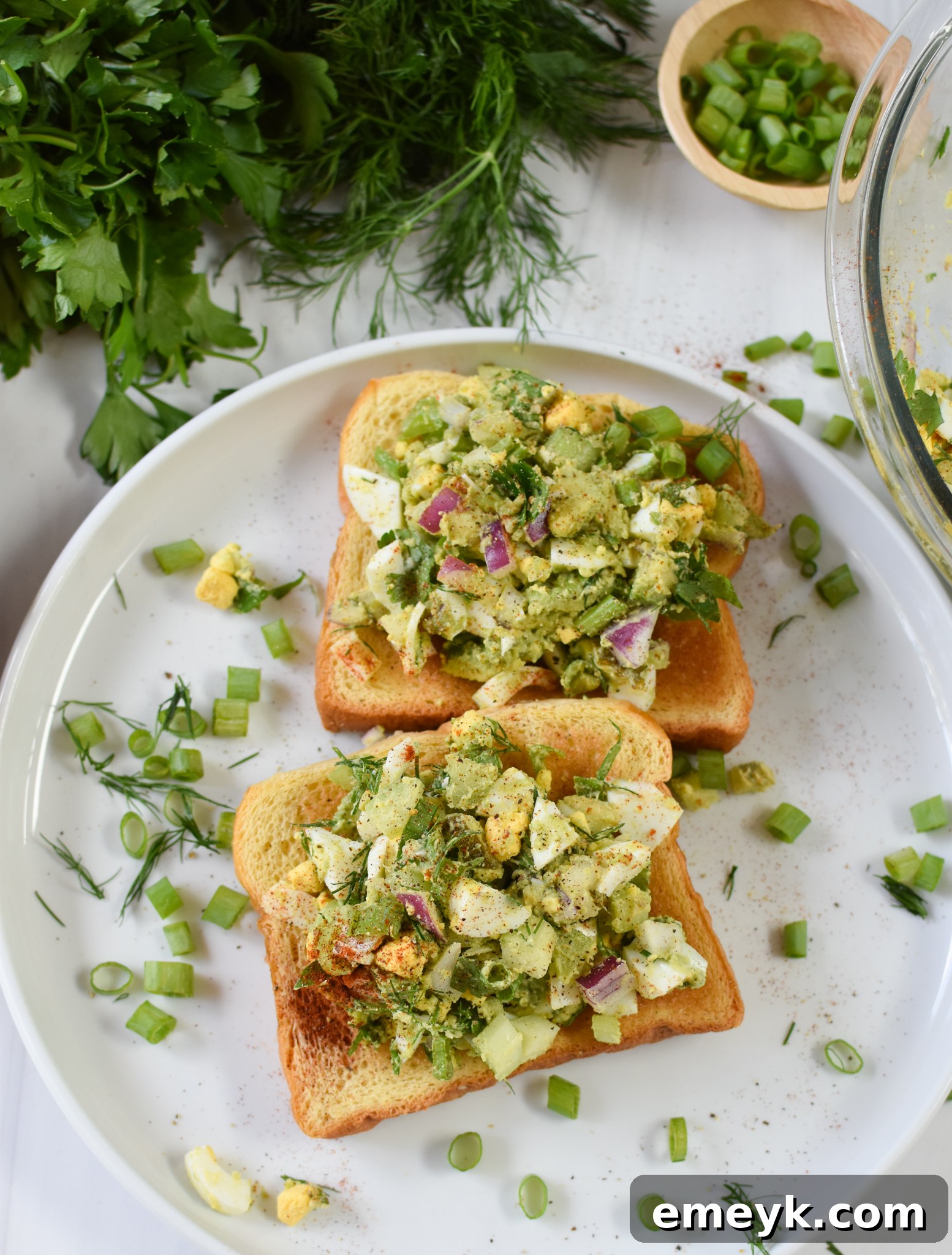 A perfectly portioned single serving of Avocado Egg Salad on a pristine white plate, elegantly garnished with a sprig of fresh herbs for a touch of vibrancy.