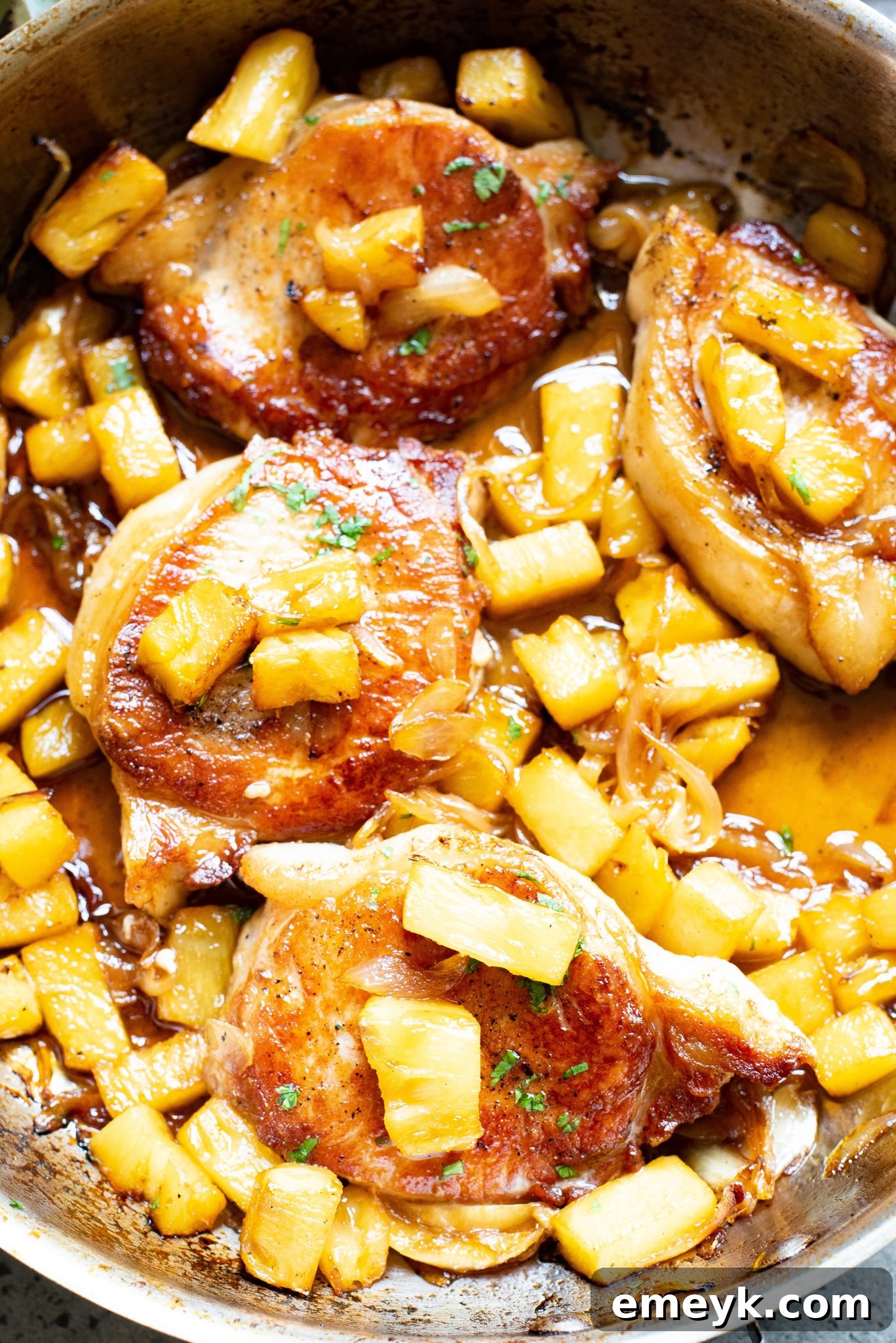 A close-up of beautifully seared easy pineapple pork chops nestled in a vibrant sauce with pineapple chunks and sliced onions in a rustic skillet, ready to be served.
