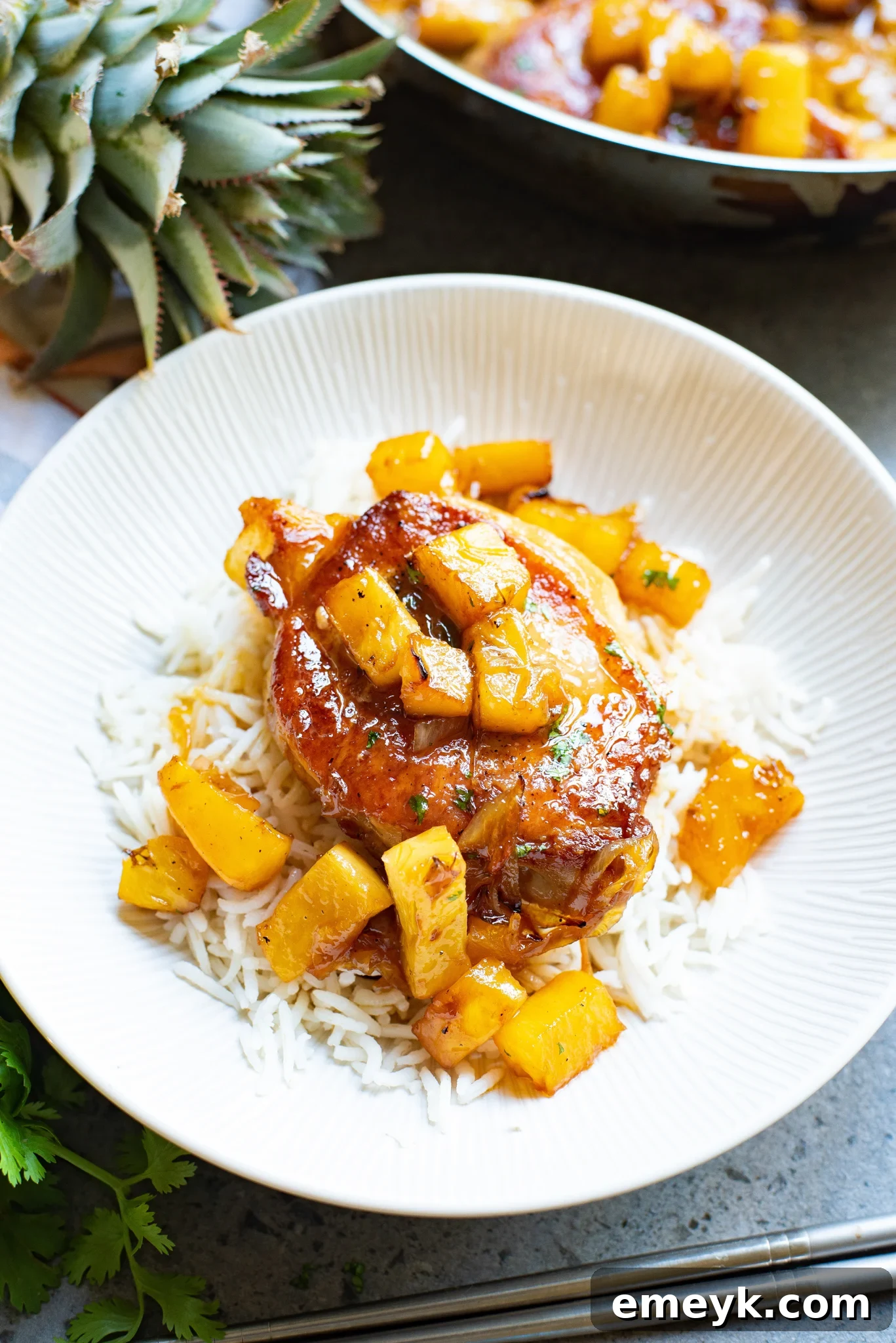 A single serving of easy pineapple pork chops, garnished with fresh cilantro, resting on a bed of white rice on a clean white plate, with extra pineapple chunks on the side.