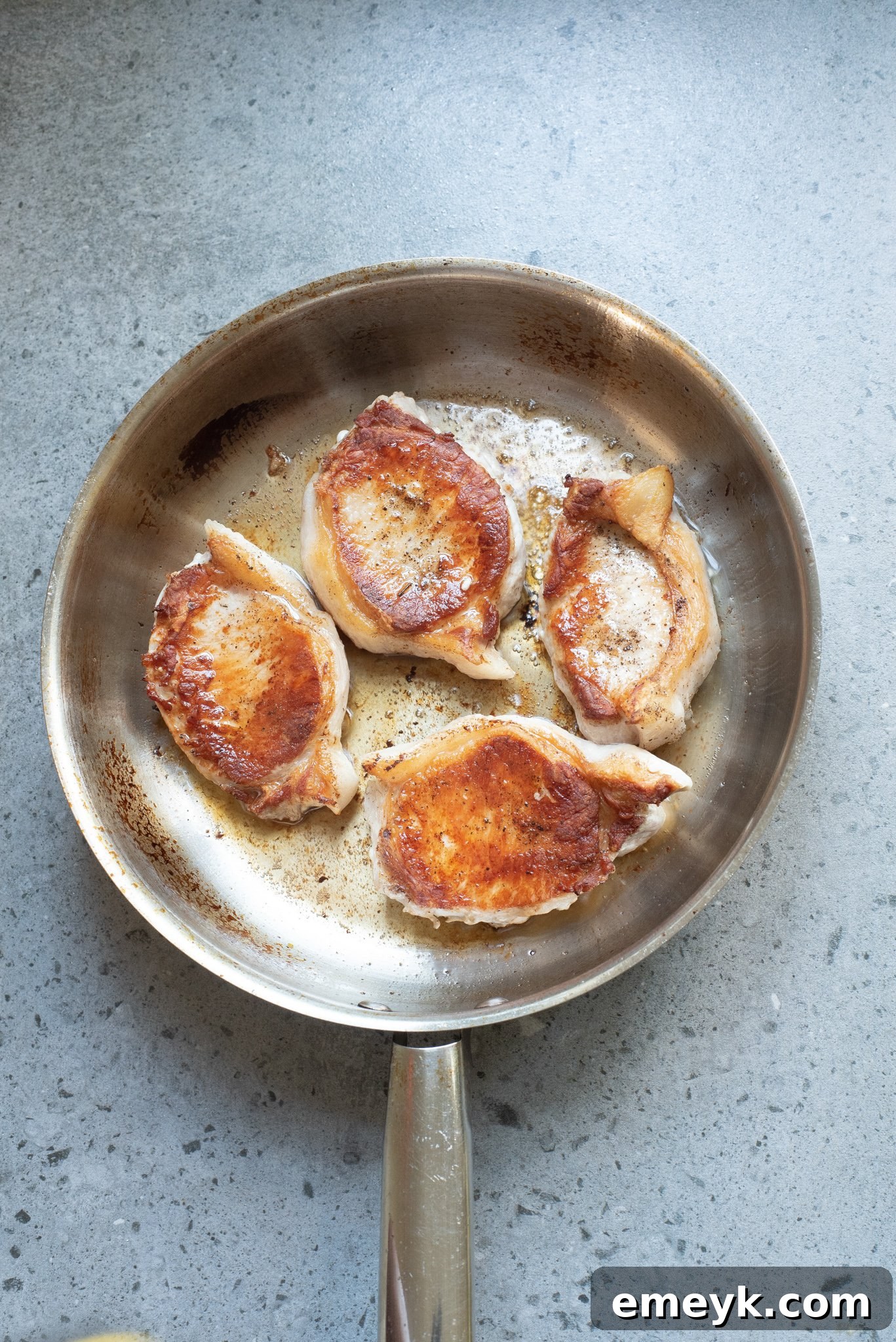 Pork chops flipped to sear on the second side, sharing the skillet with sautéing onions and garlic, creating a flavorful base for the pineapple sauce.