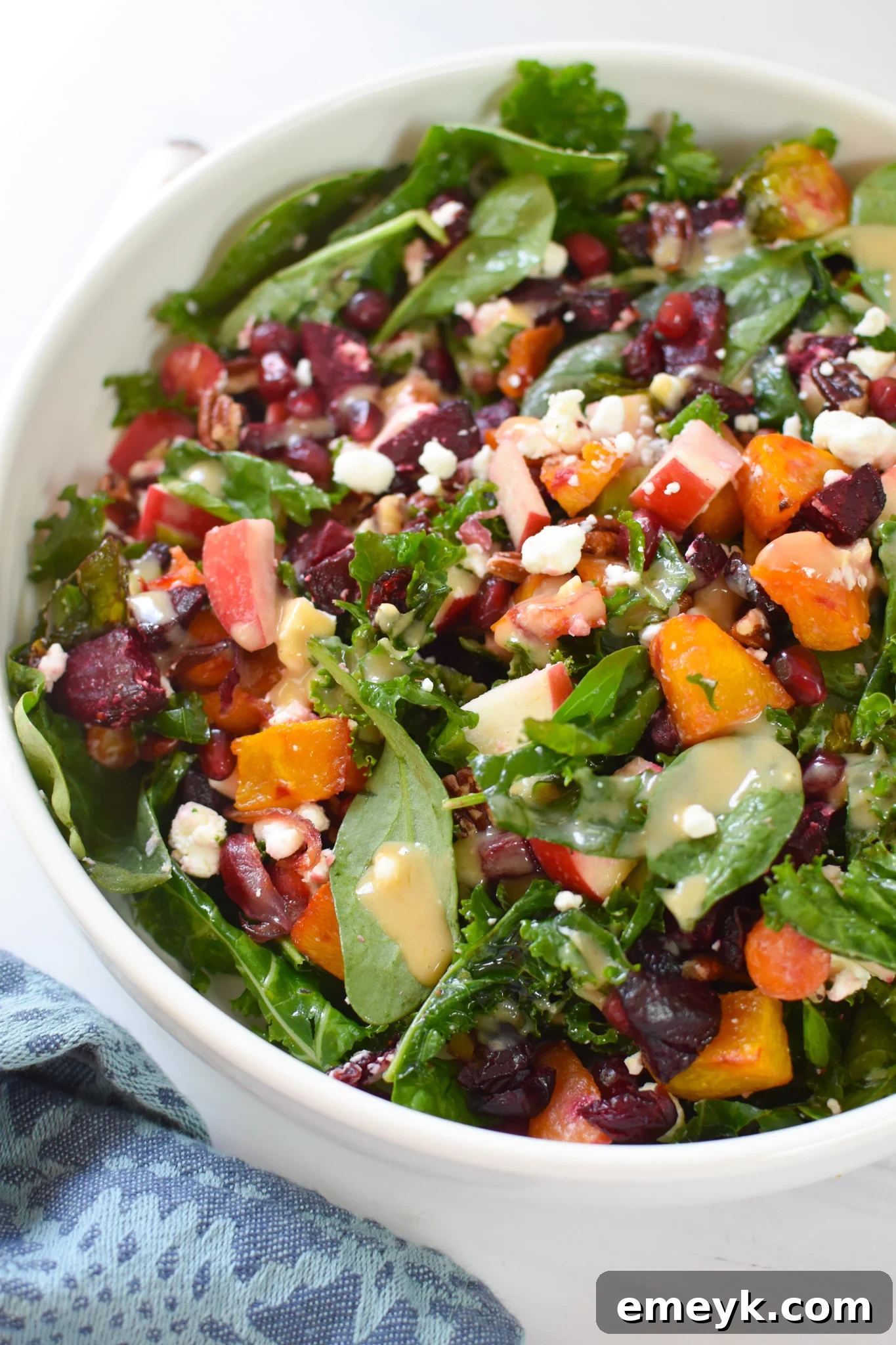 A beautifully arranged Fall Harvest Salad in a white bowl, showcasing roasted vegetables, green leaves, and colorful toppings.