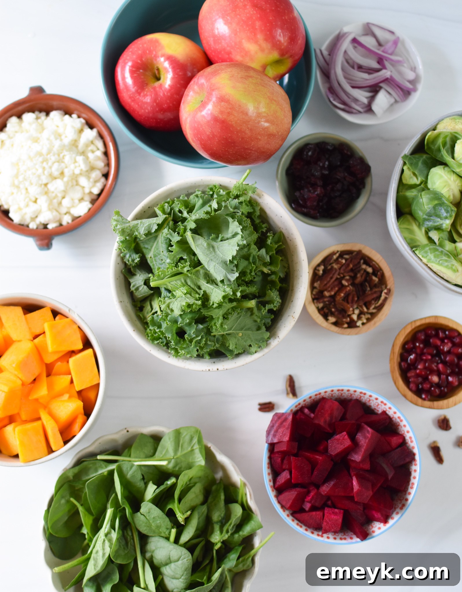 Fresh ingredients for a Fall Harvest Salad laid out on a table, including butternut squash, beets, Brussels sprouts, kale, spinach, and other colorful components.