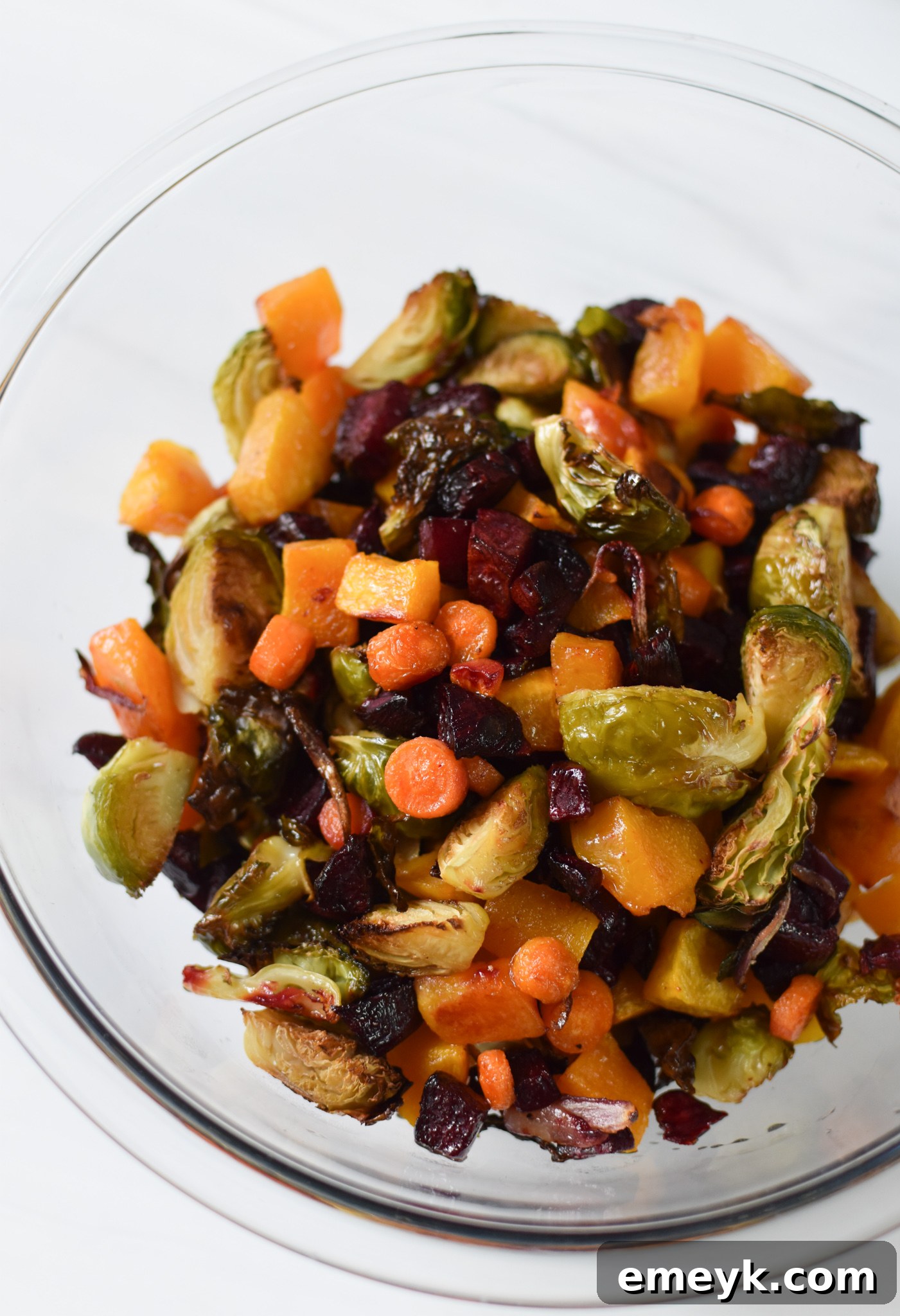 Close-up of roasted vegetables, including butternut squash, Brussels sprouts, beets, carrots, and red onion, on a baking sheet.