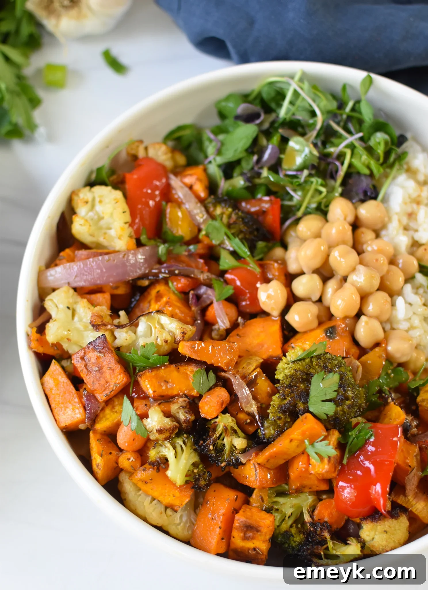 A vibrant Sweet Potato Bowl, showcasing roasted sweet potatoes, colorful vegetables, grains, greens, and chickpeas, drizzled with tahini dressing.